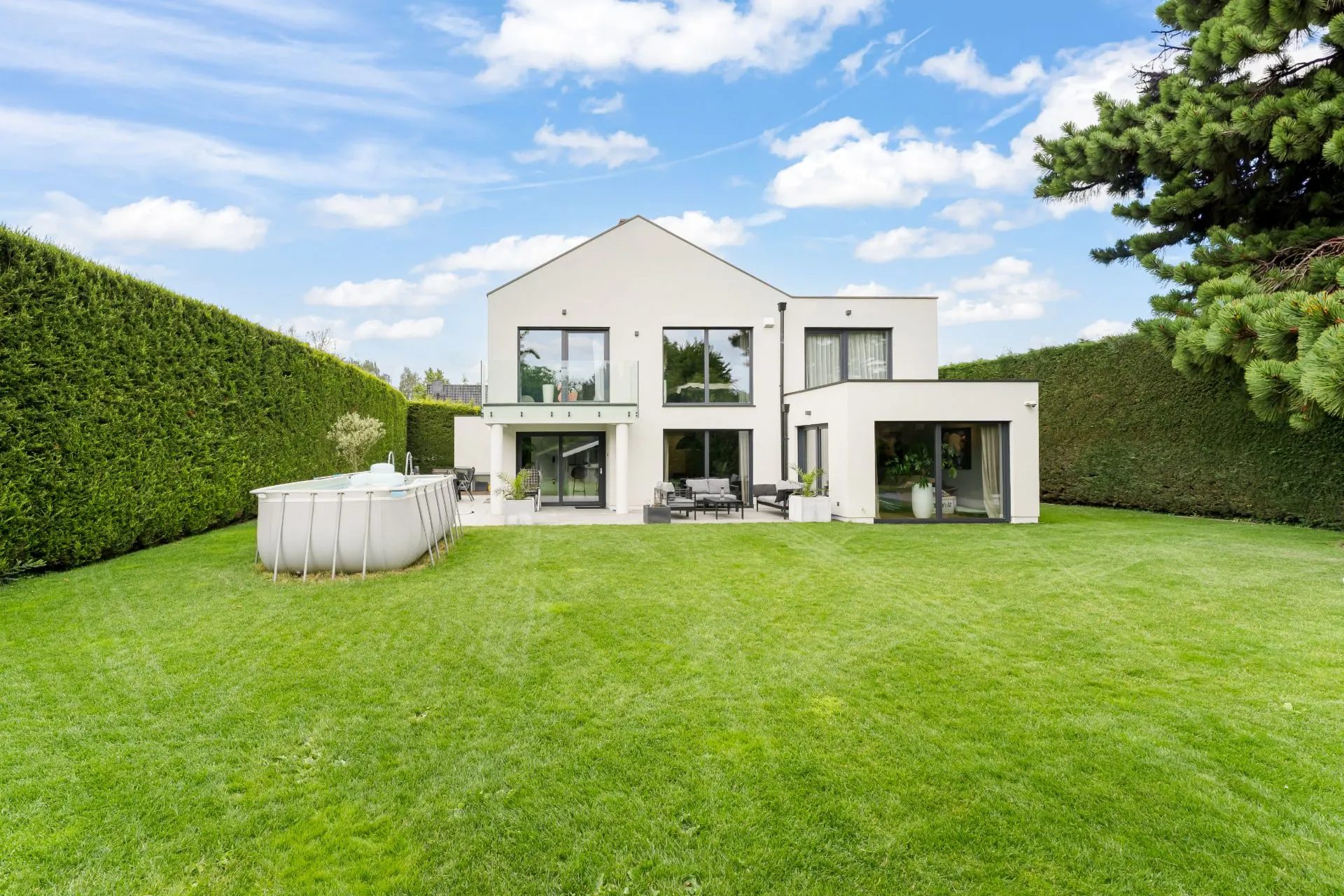 Modernes Einfamilienhaus mit großem Garten, Terrasse und Pool, umgeben von hohen Hecken.