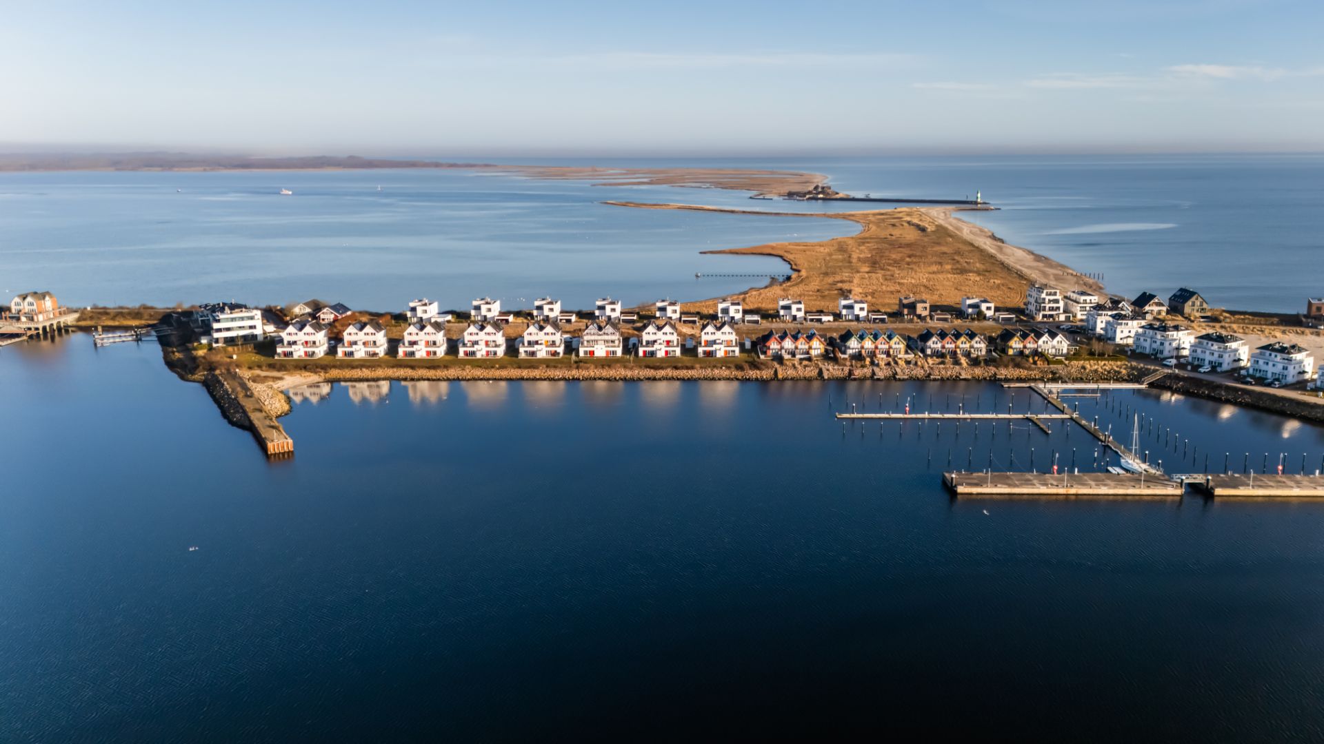 Luftaufnahme von Häuserreihen am Wasser mit kleiner Landzunge im Hintergrund.
