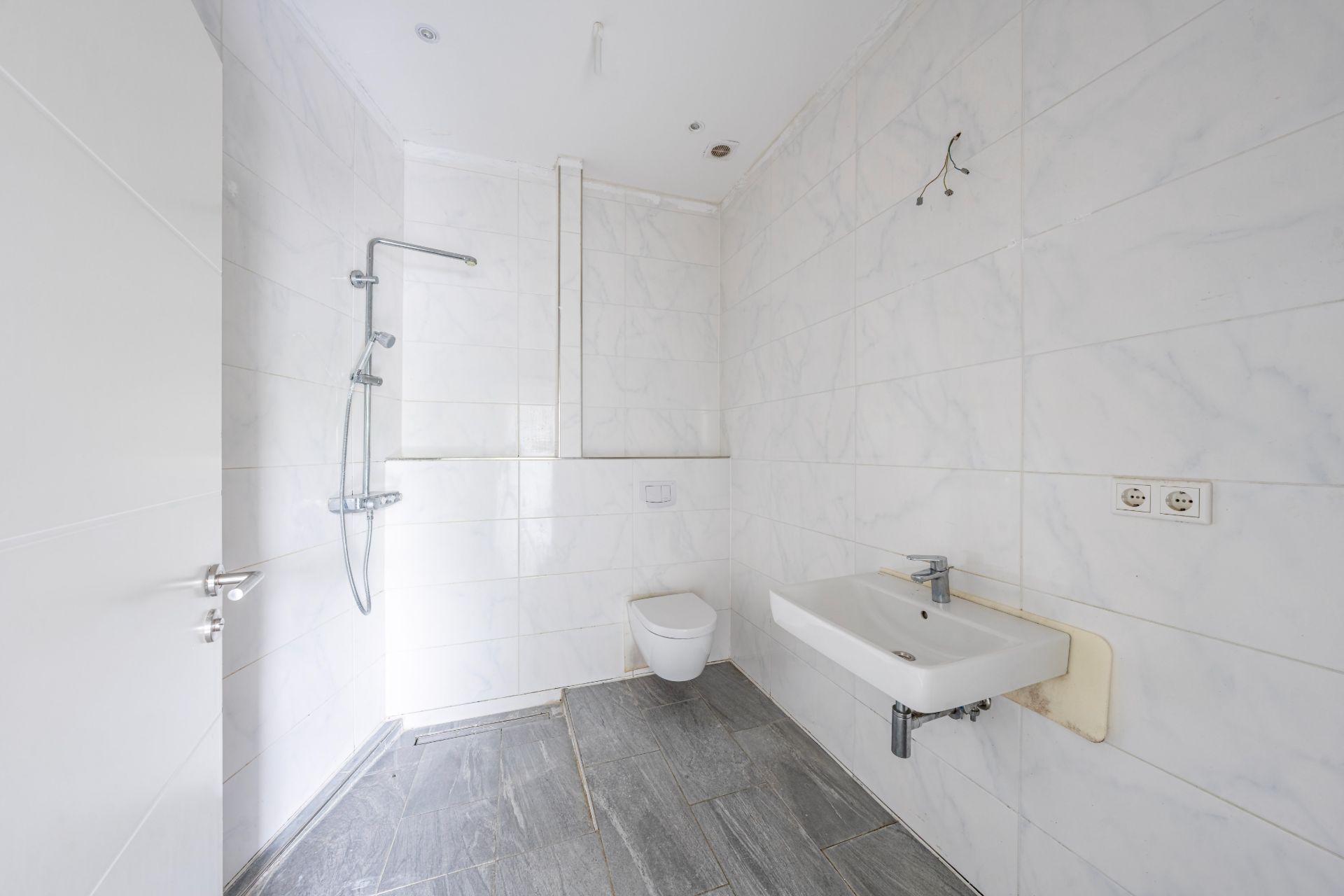 Modernes, weiß gefliestes Badezimmer mit Dusche, Wandtoilette und Waschbecken.