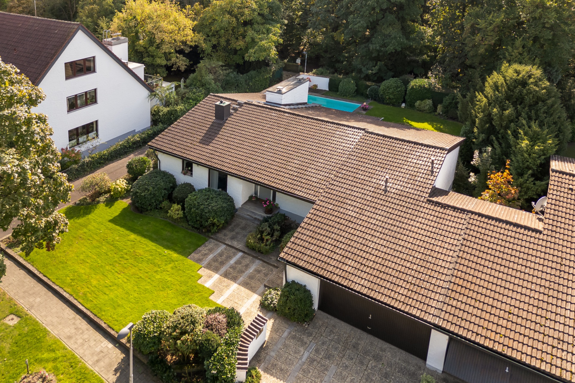 Luftaufnahme eines Einfamilienhauses mit Garten, Garage und Swimmingpool im Hintergrund.