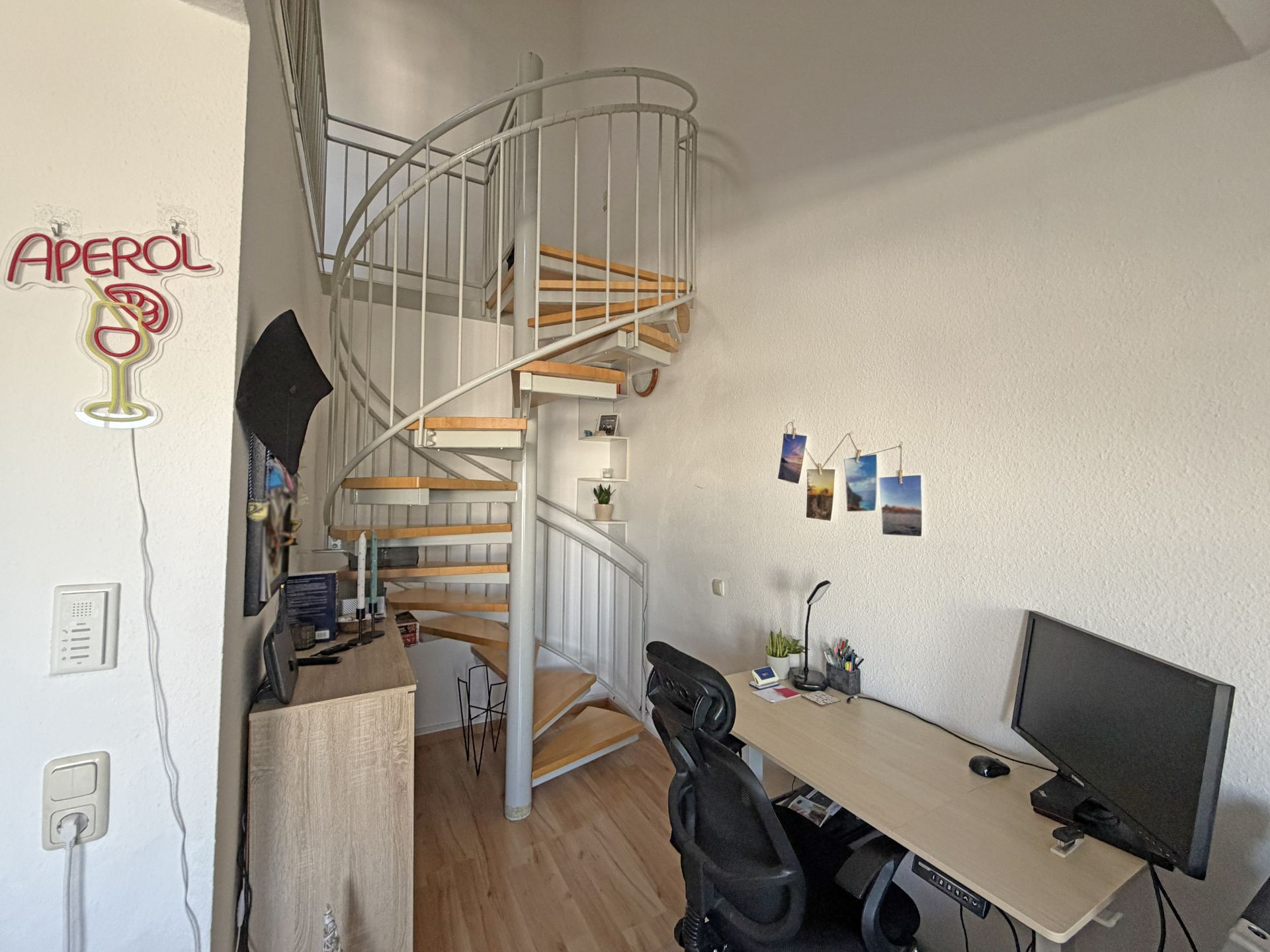Zimmer mit Holz-Spiraltreppe, Schreibtisch, Bürostuhl und Dekoration an der Wand.