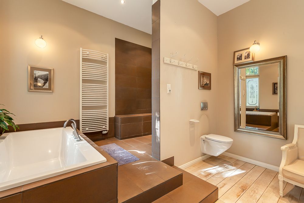 Modernes Badezimmer mit Badewanne, hängender Toilette, großem Spiegel und Handtuchheizkörper.