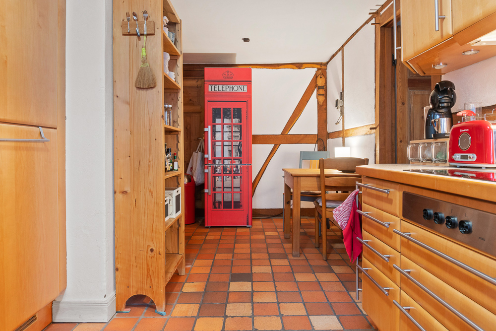 Küche mit Holzmöbeln und rotem Telefonzellen-Kühlschrank, Esstisch im Hintergrund.