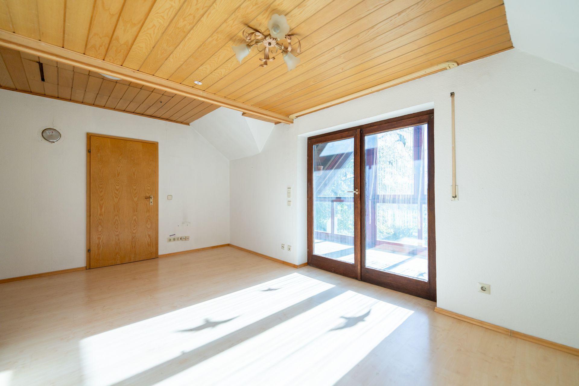 Heller leerer Raum mit Holzboden, Holzdecke, Tür und großen Fenstern mit Balkonzugang.