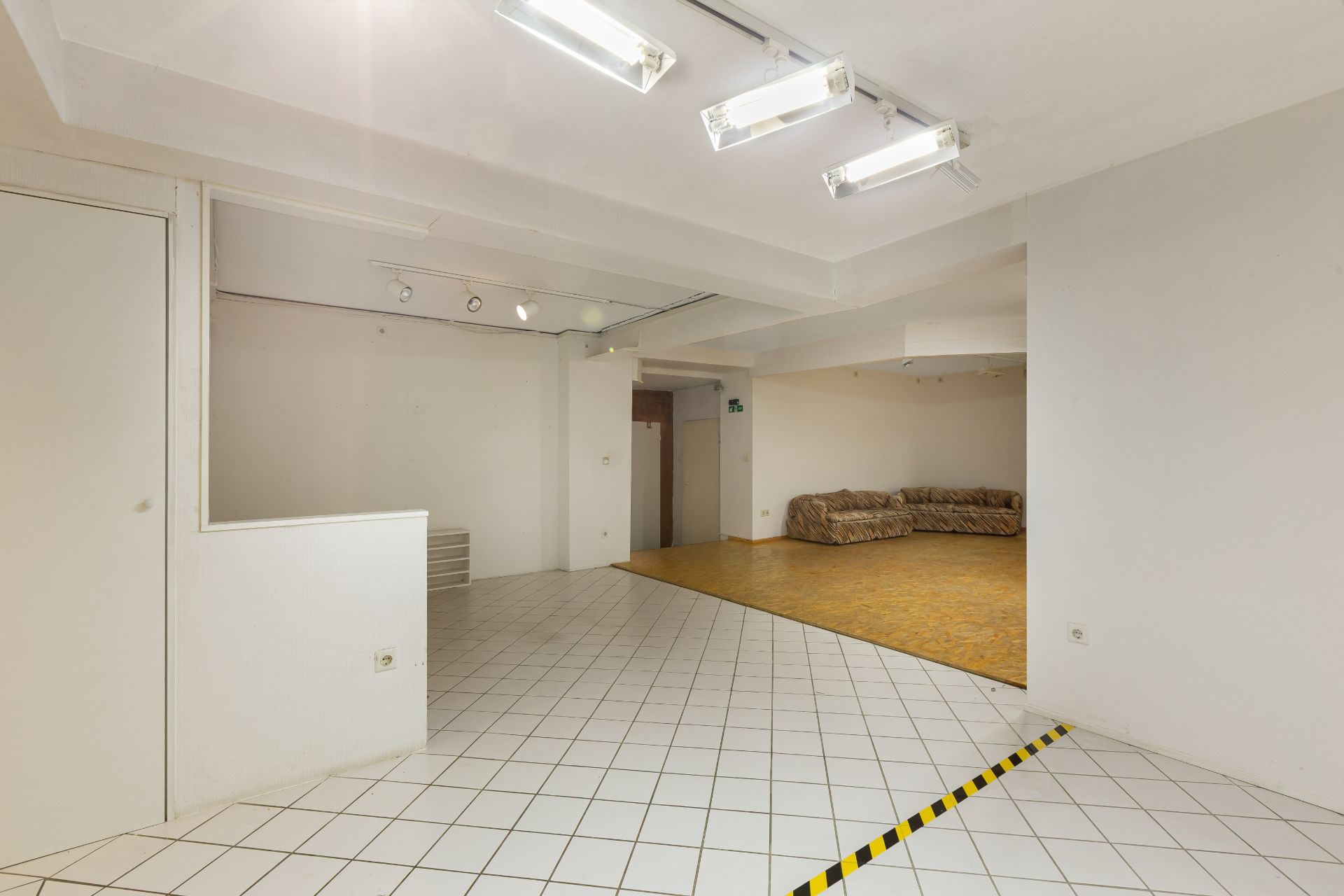 Großer Raum mit weißen Fliesen, Holzfläche im Hintergrund und zwei Sofas an der Wand.