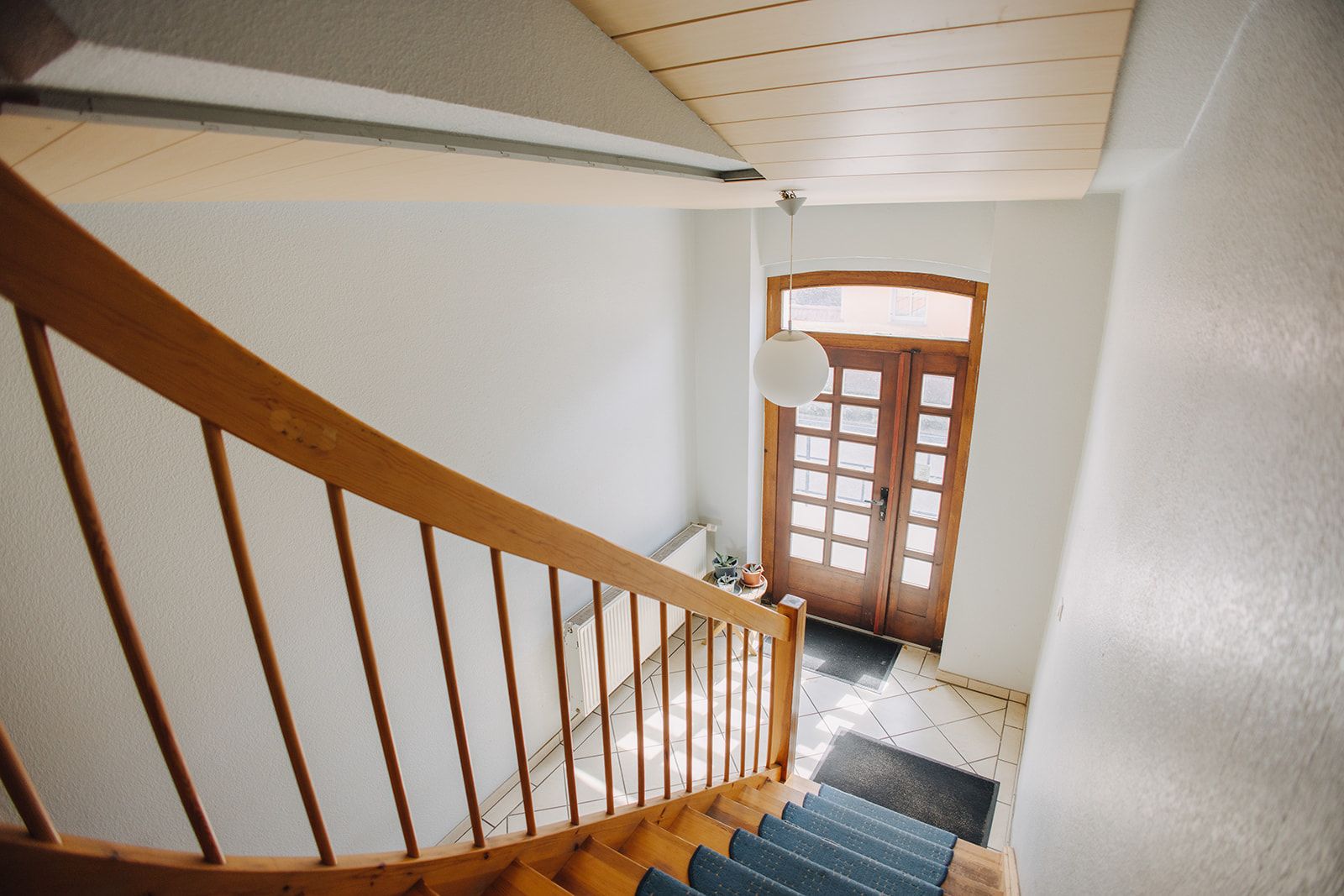 Heller Eingangsbereich mit Holztreppe, Fliesenboden und einer Holztür mit Glasscheiben.