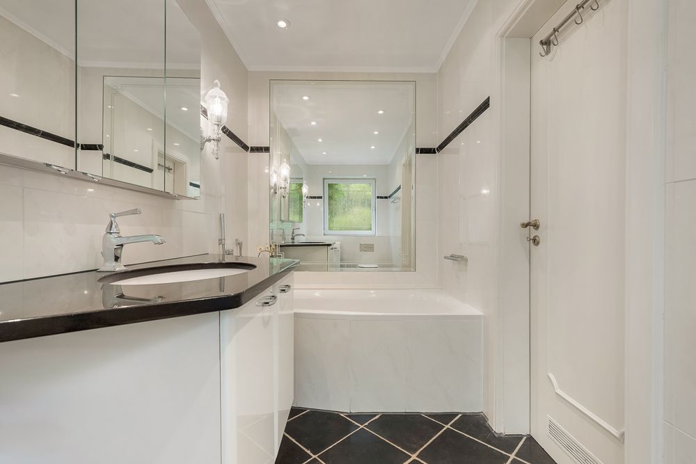 Modernes Badezimmer mit Badewanne, großem Spiegel, Waschbecken und Fenster.