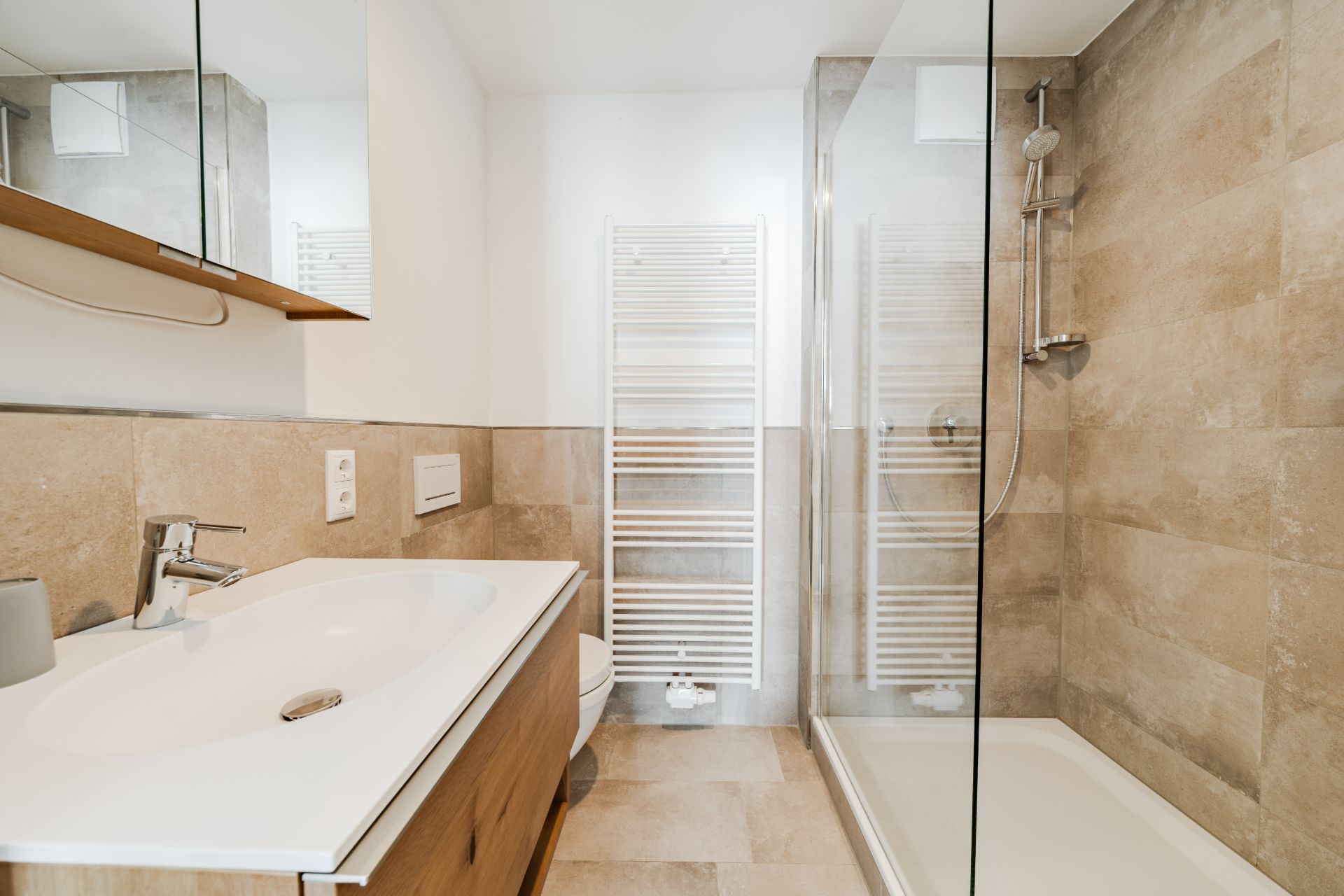 Modernes Badezimmer mit Dusche, Waschbecken, Spiegel, WC und Heizkörper.