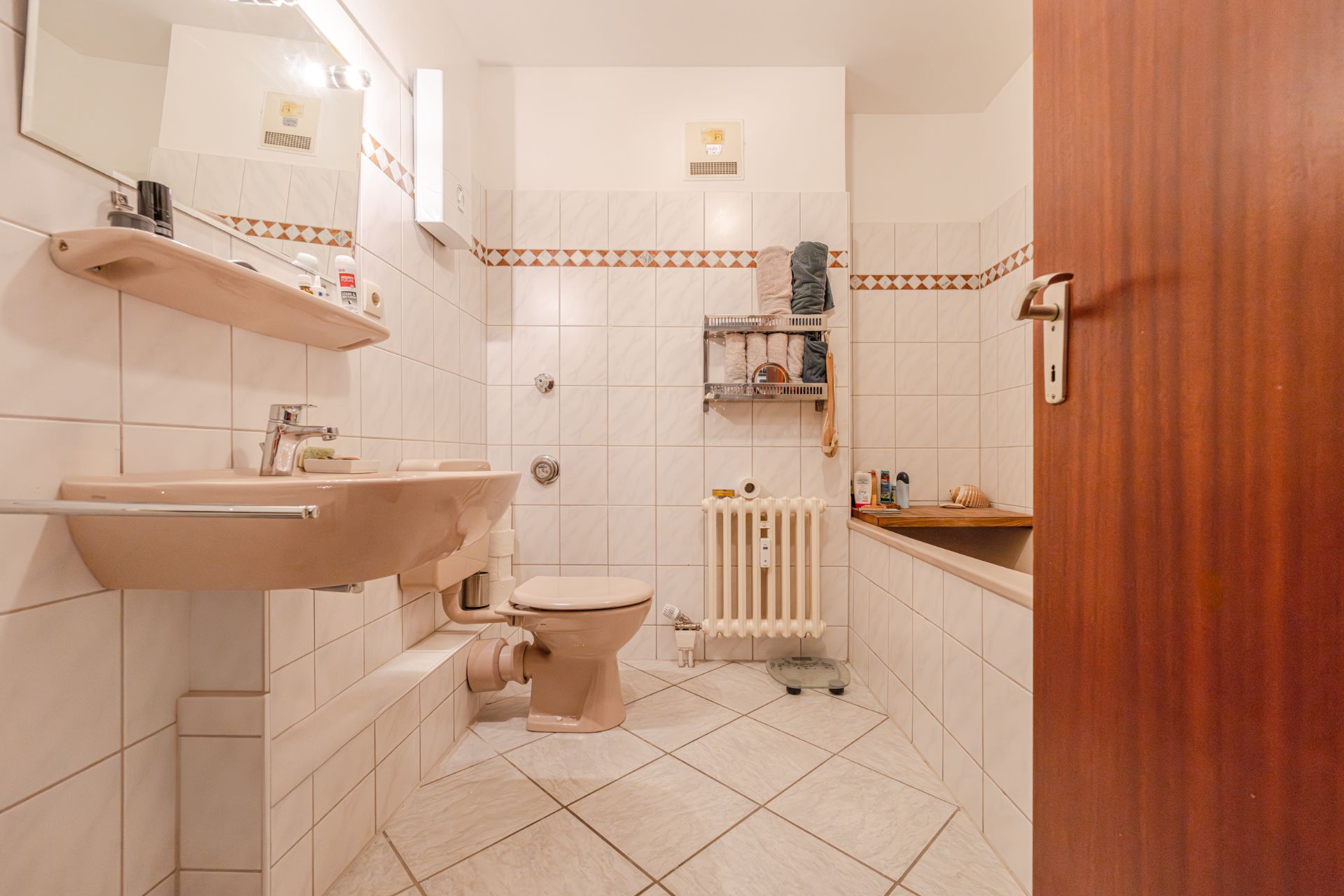 Beiges Badezimmer mit Waschbecken, Toilette, Badewanne und Regal mit Handtüchern.