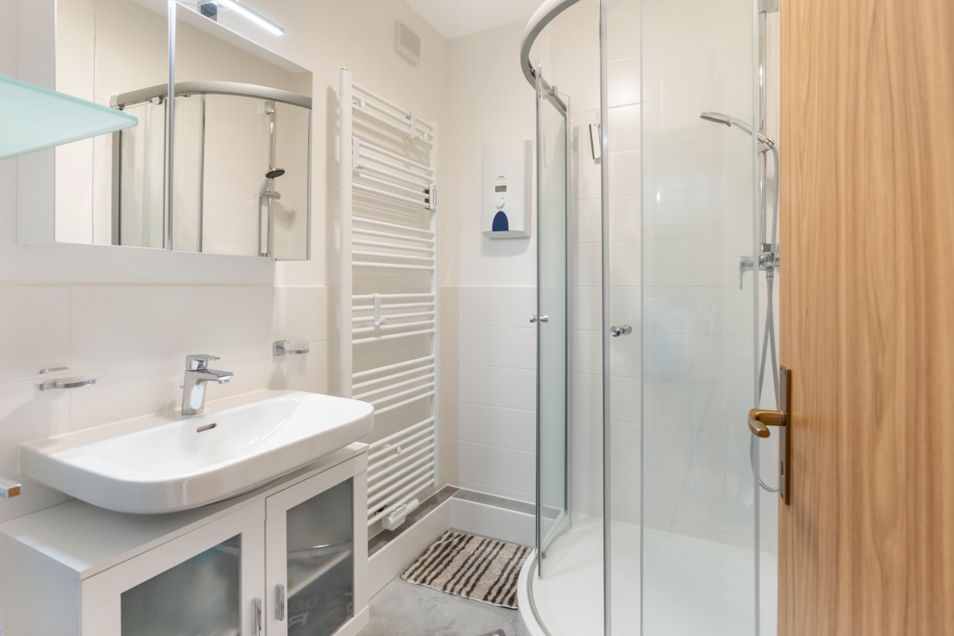 Modernes Badezimmer mit Waschbecken, Spiegel, Handtuchheizkörper und runder Dusche.