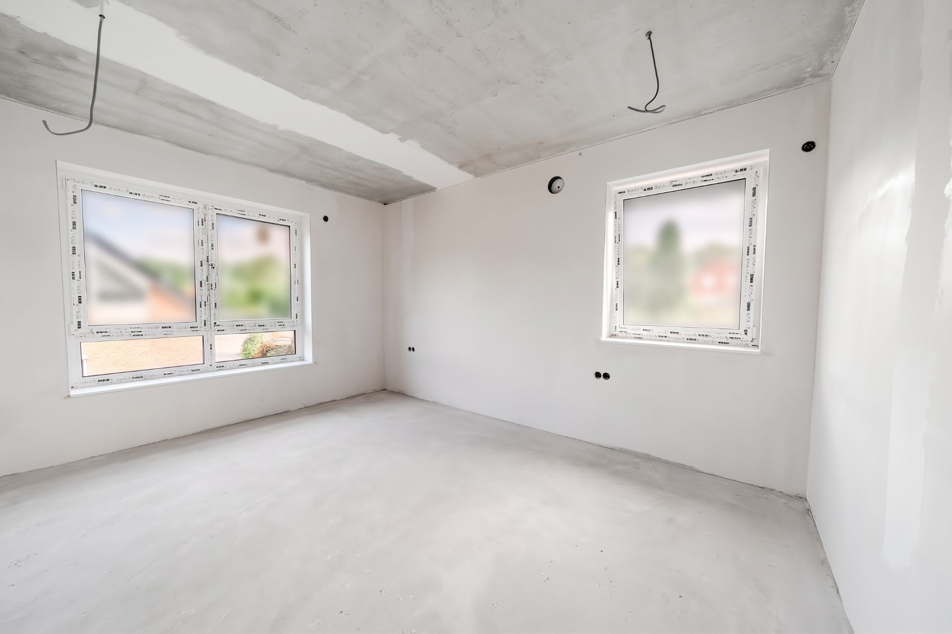 Heller, leerer Raum mit weißen Wänden, zwei Fenstern und unverputzter Decke.