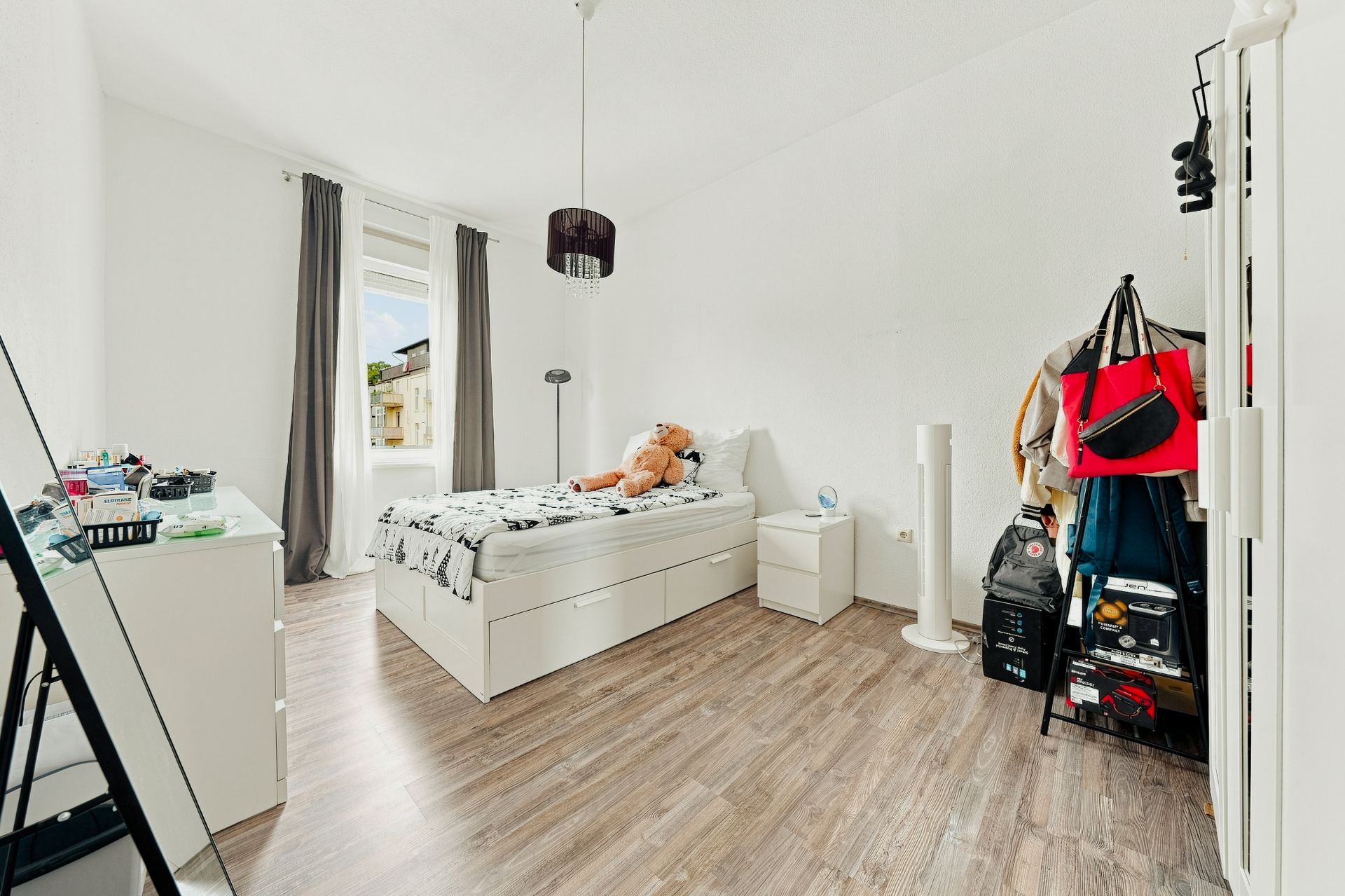Helles Schlafzimmer mit Einzelbett, Nachttisch, Kommode, Kleiderständer und Holzfußboden.