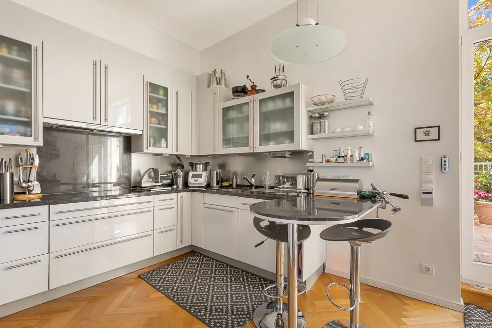 Moderne, helle Küche mit weißen Schränken, Kücheninsel und zwei Barhockern.