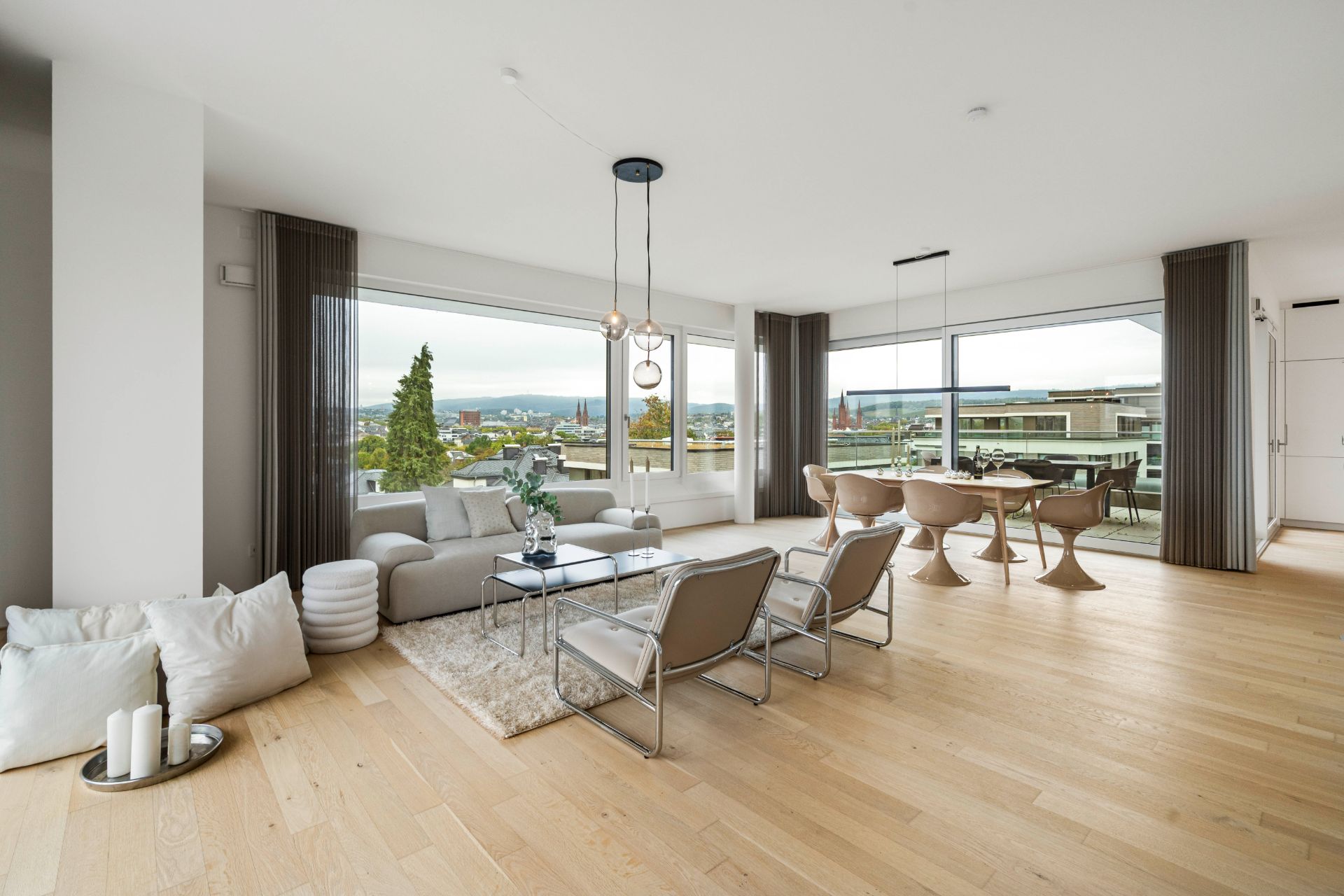 Helles Wohnzimmer mit Sofaecke, Esstisch und großen Fenstern mit Stadtblick.