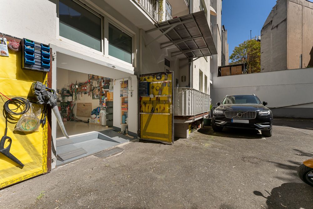 Offene Garage mit Werkzeugen an der Wand, daneben parkt ein schwarzes Auto im Hof.