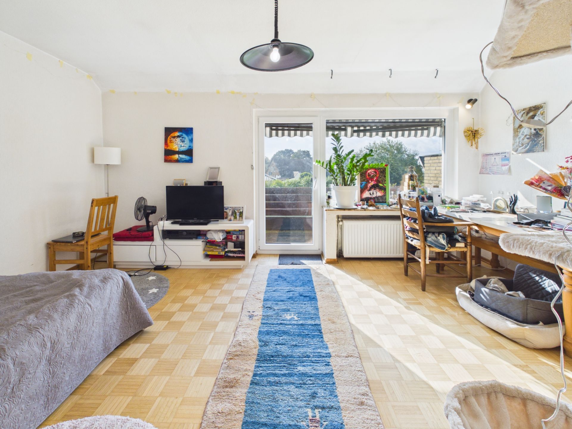 Helles Wohnzimmer mit Sofa, Schreibtisch, Teppich und Zugang zu einem Balkon.