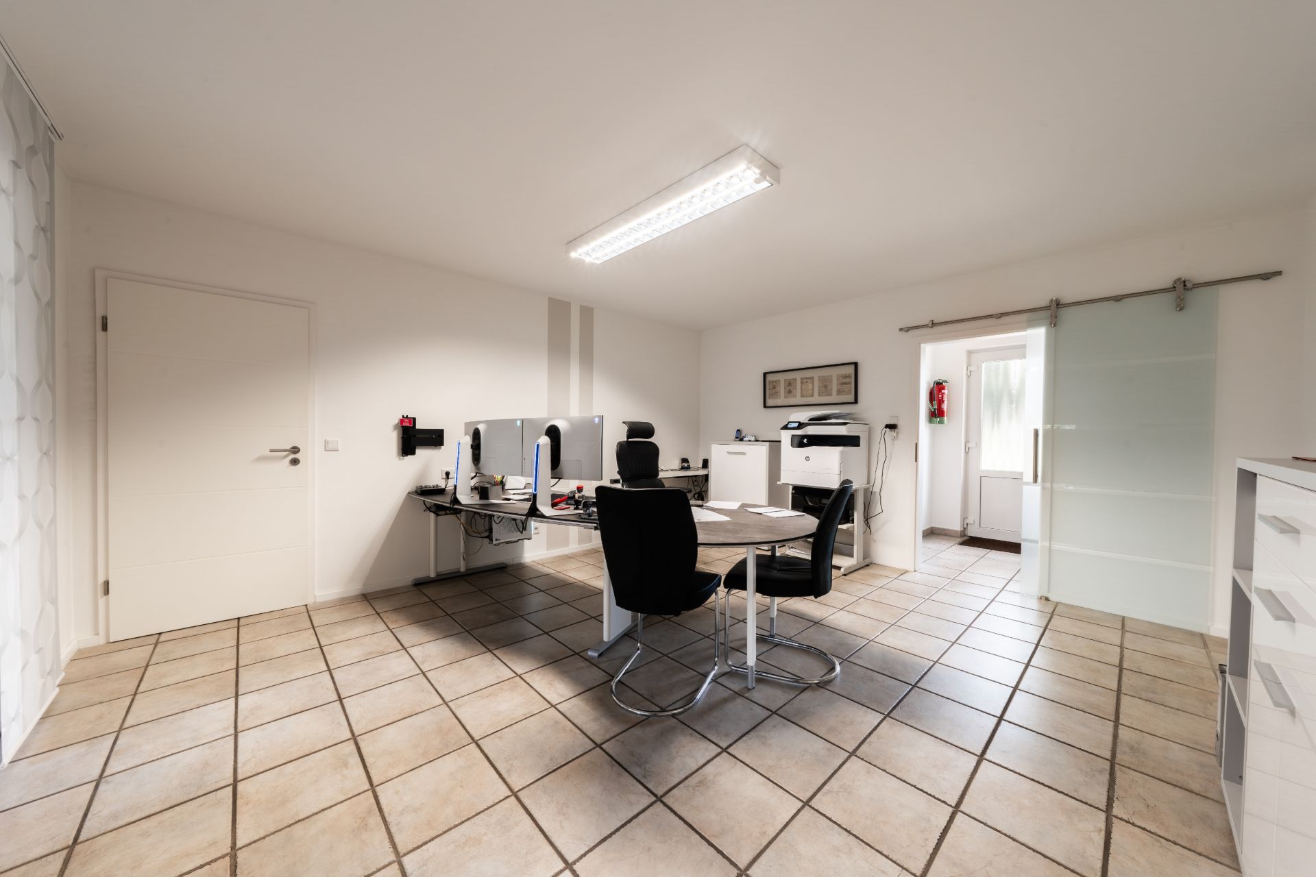 Helles Arbeitszimmer mit zwei Schreibtischen, Computern und Stühlen auf gefliestem Boden.