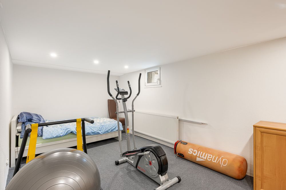 Zimmer mit Bett, Fitnessgeräten, Gymnastikball und kleinem Fenster an der Wand.