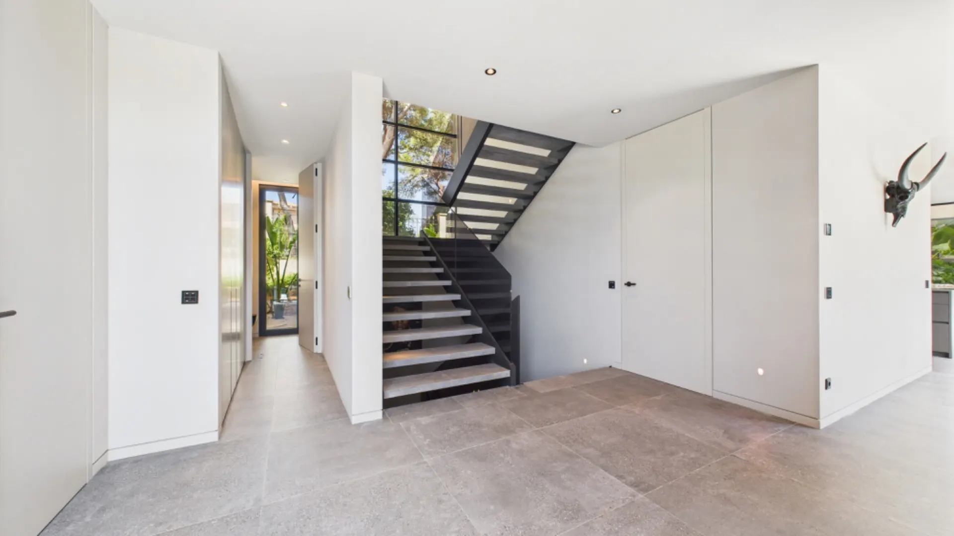 Heller Flur mit moderner Treppe, großen Fliesen und Wanddekoration in einem Wohnhaus.