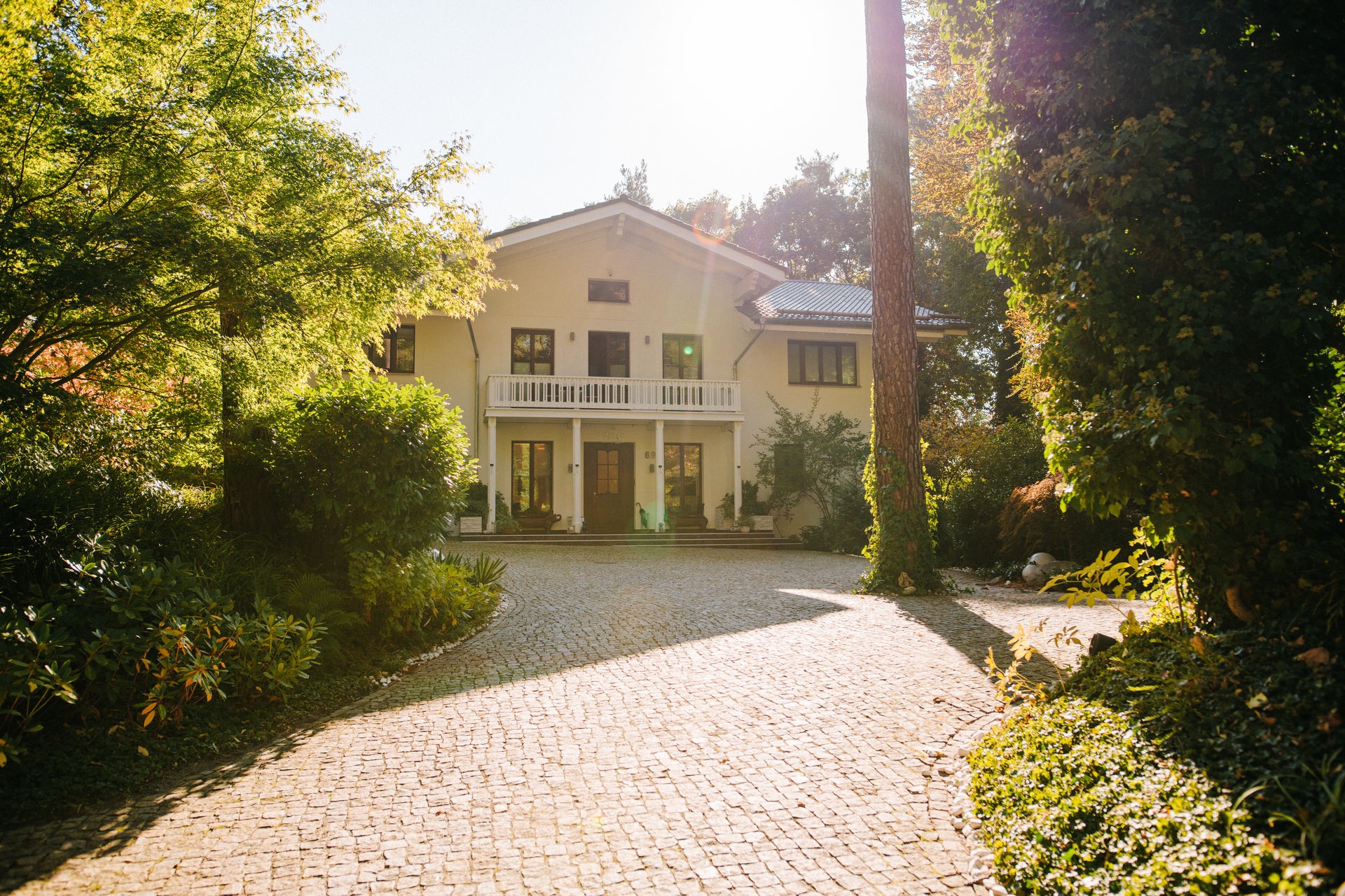 Zweistöckiges Wohnhaus mit Balkon und gepflasterter Einfahrt im Grünen.