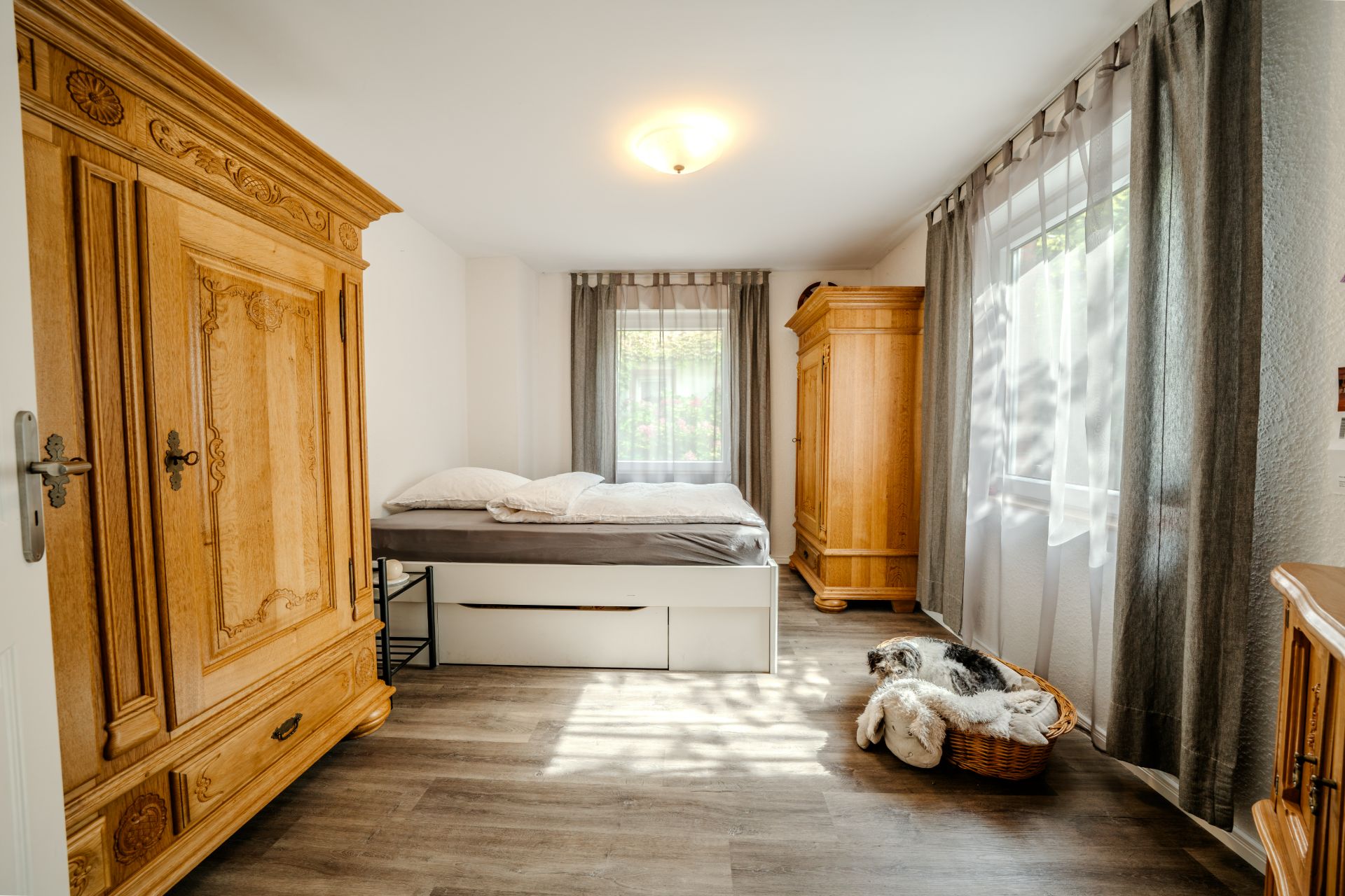 Helles Schlafzimmer mit Holzboden, Bett, zwei Kleiderschränken und Fenster mit Vorhängen.