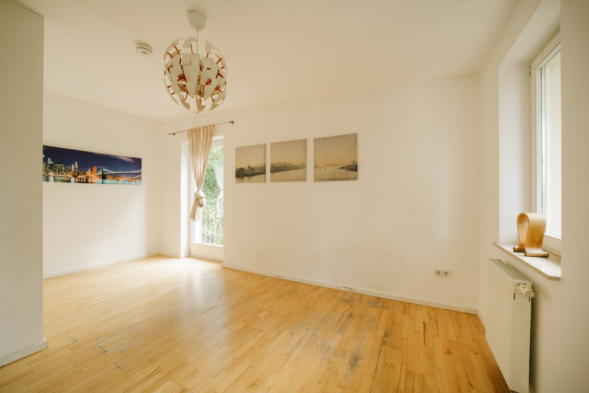 Helles Wohnzimmer mit Holzfußboden, weißen Wänden, Fenstern und Wandbildern.