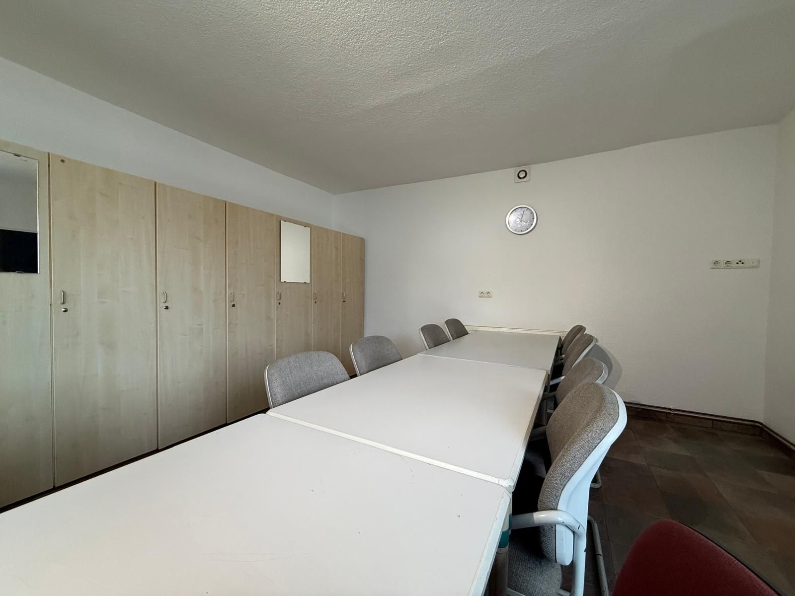 Raum mit langem Tisch, mehreren Stühlen und hellen Schränken an der Wand.