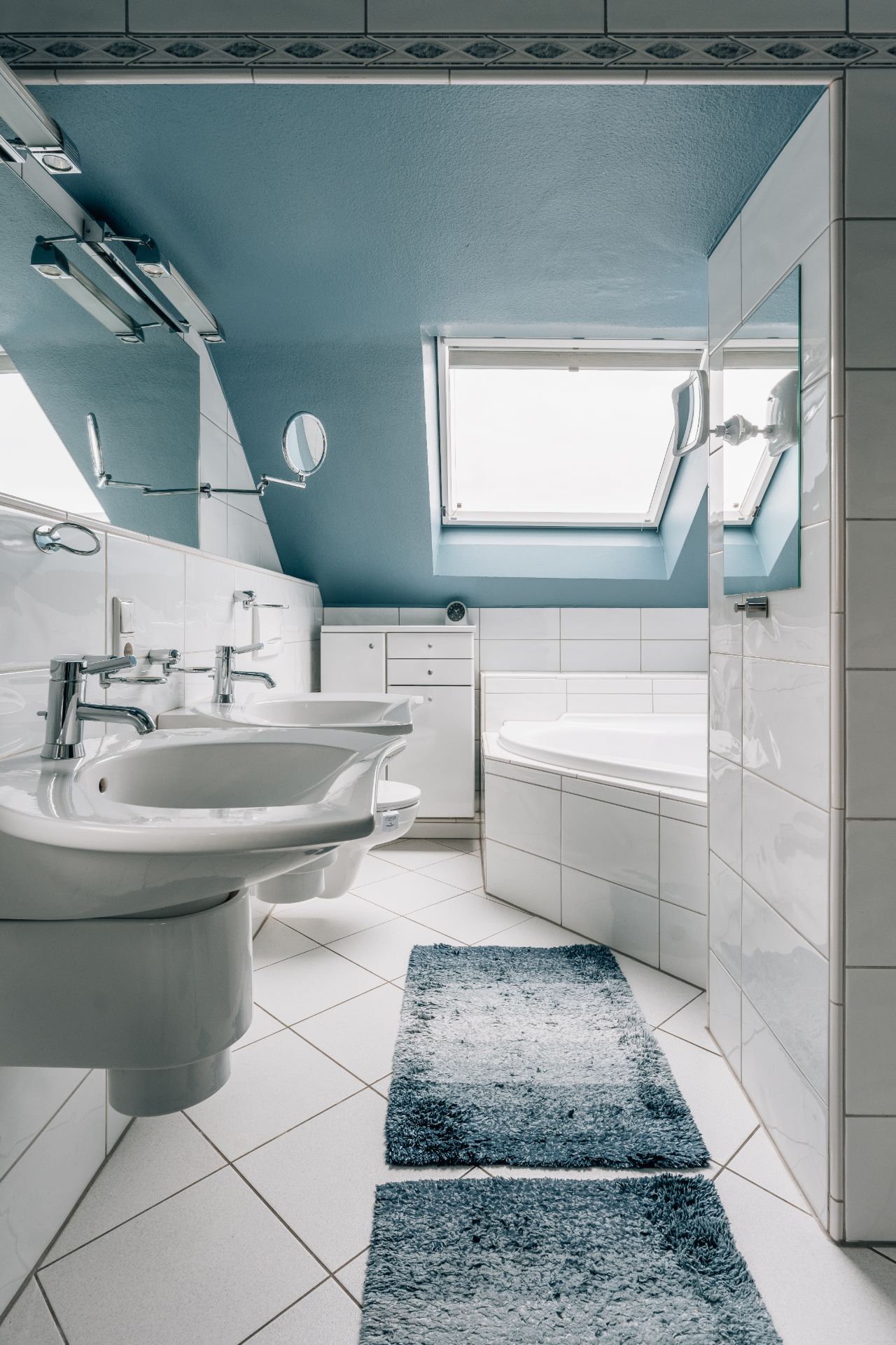 Modernes Badezimmer mit zwei Waschbecken, Badewanne, Spiegeln und Dachfenster.