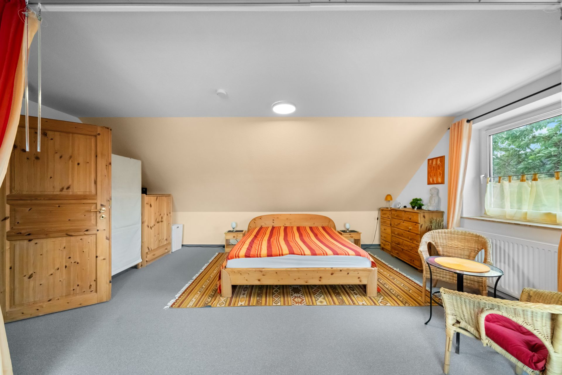 Gemütliches Schlafzimmer mit Holzbett, Schränken, Sessel und großem Fenster.