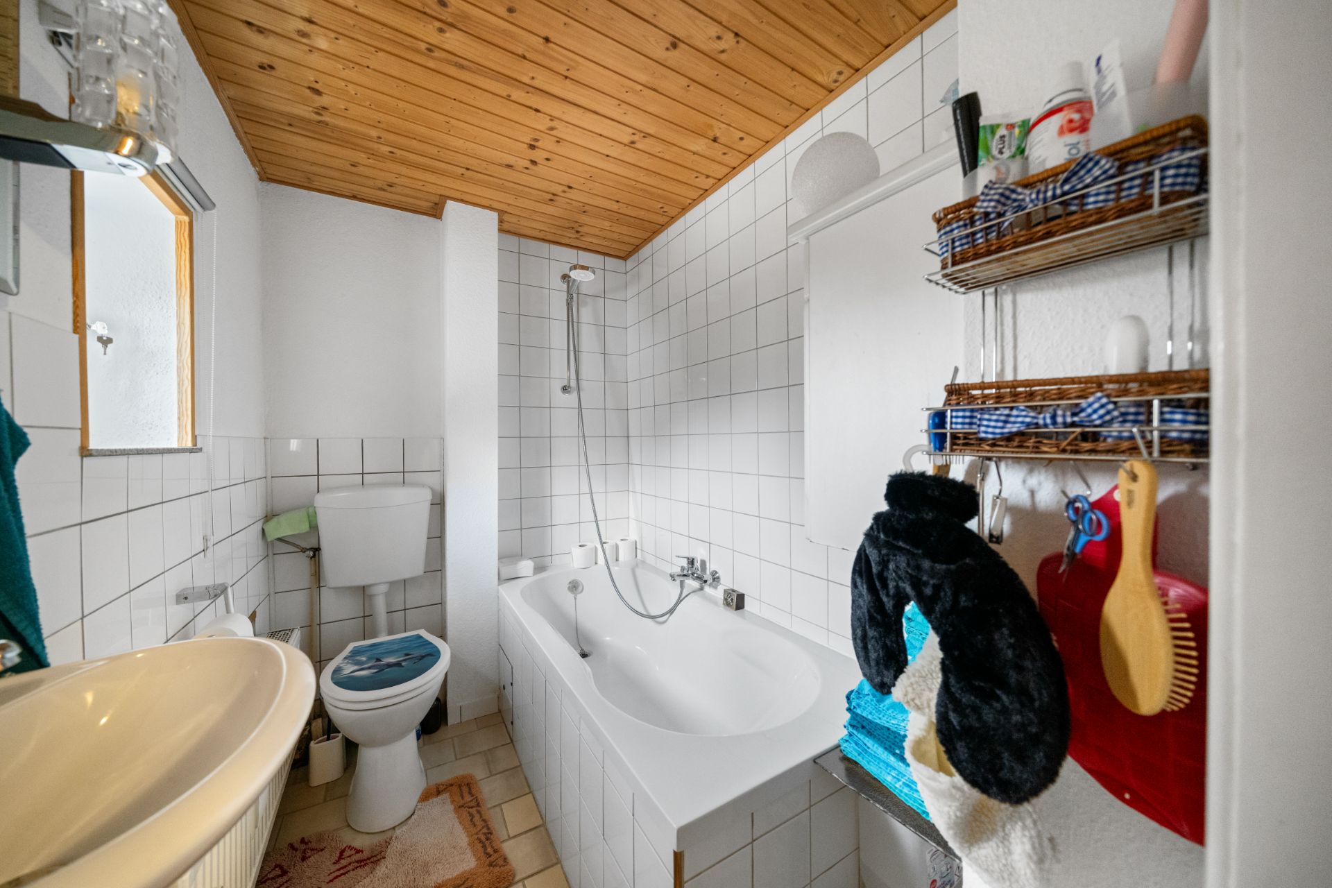 Helles Badezimmer mit Badewanne, Toilette, Waschbecken und Regalen an der Wand.