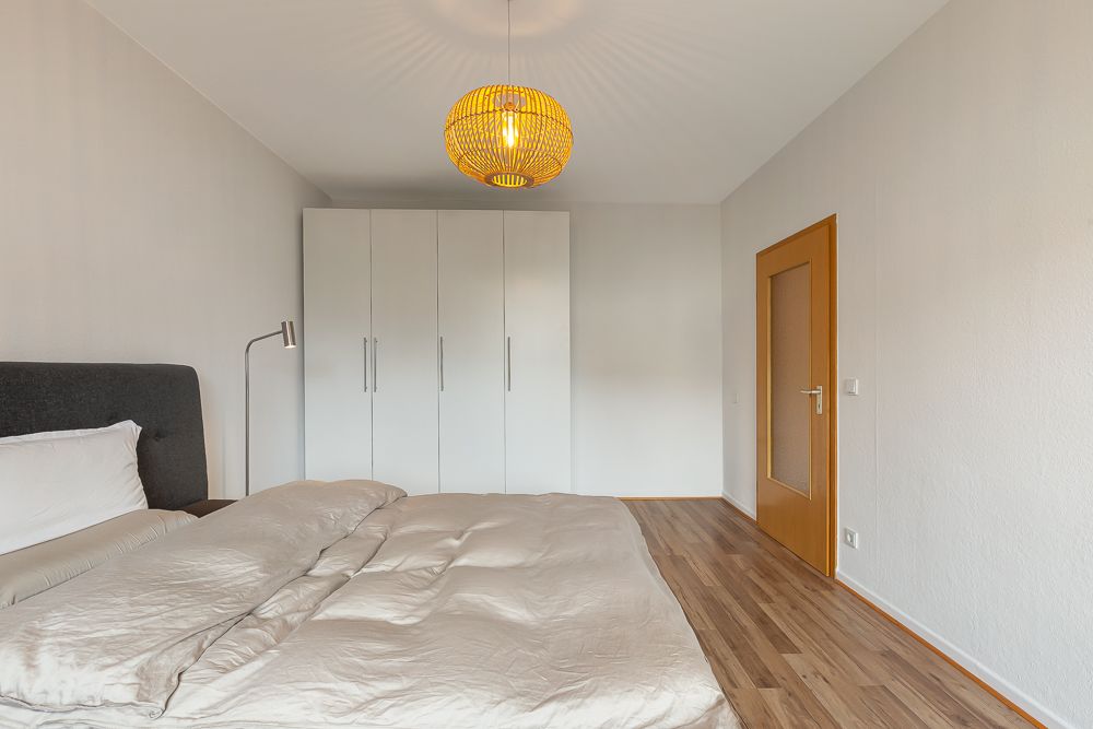 Schlafzimmer mit großem Bett, weißem Kleiderschrank und Holztür auf Laminatboden.