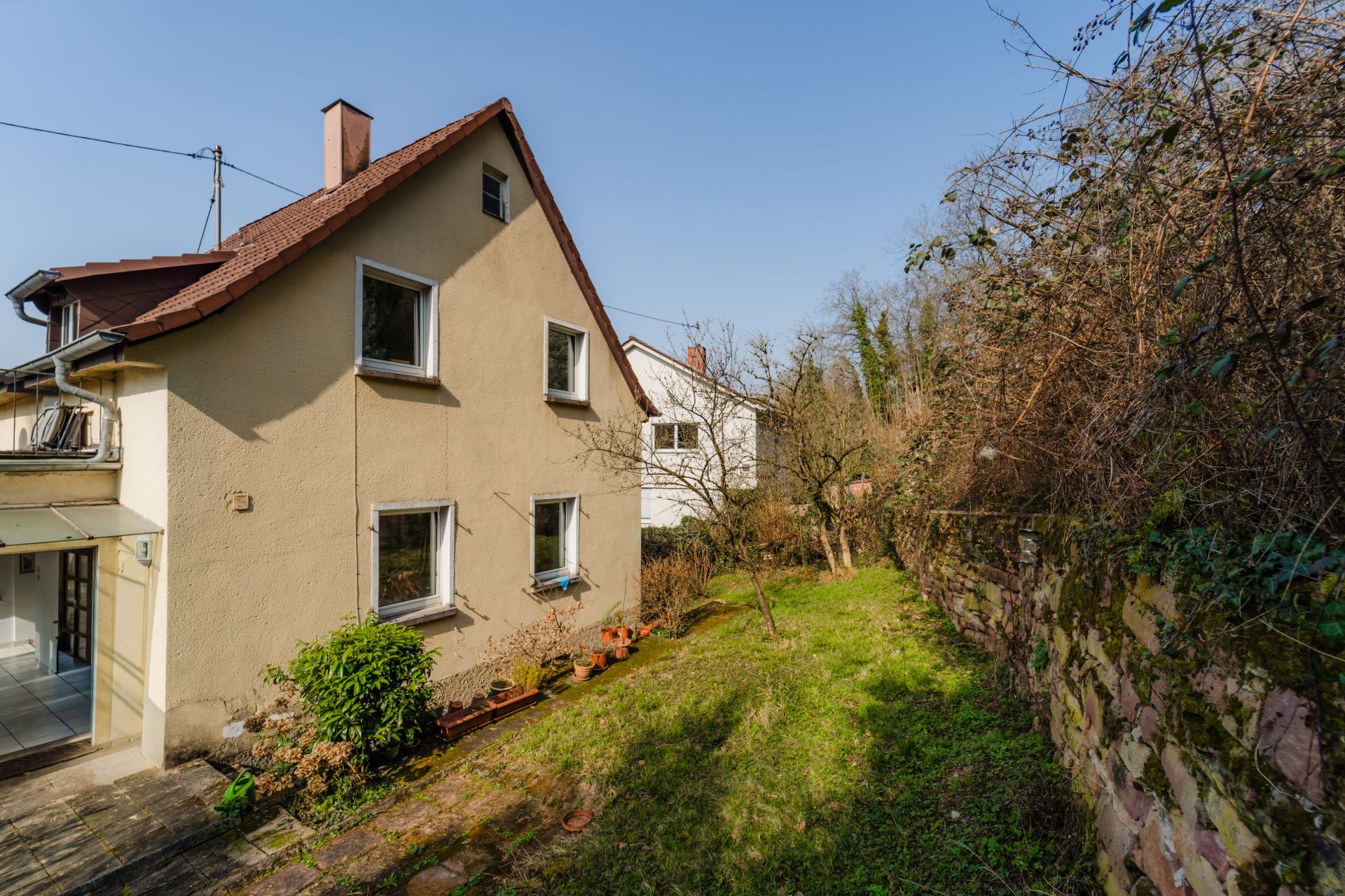 Zweistöckiges Wohnhaus mit Garten und Steinmauer an der Seite.