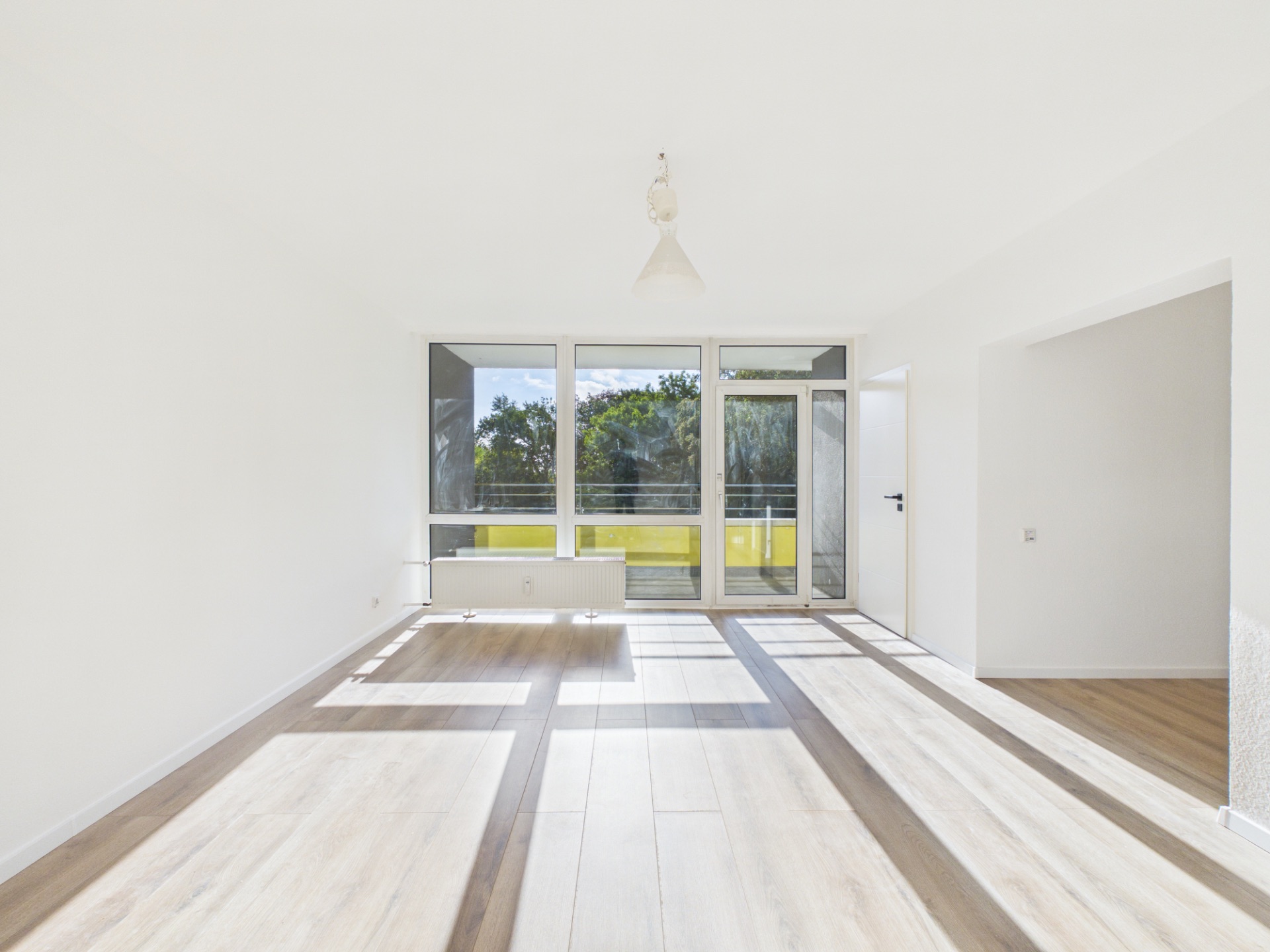 Helles Wohnzimmer mit großen Fenstern, Holzboden und Zugang zu einem Balkon.