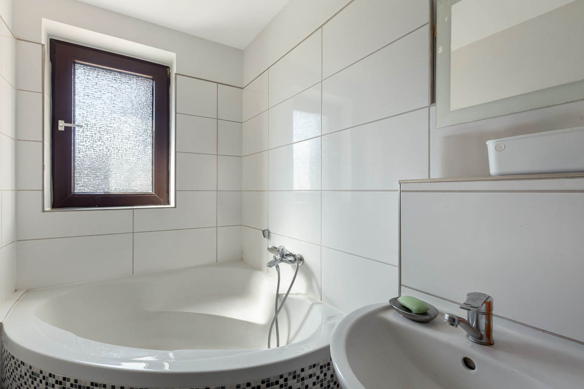 Helles Badezimmer mit Eckbadewanne, Waschbecken und Fenster mit Milchglas.