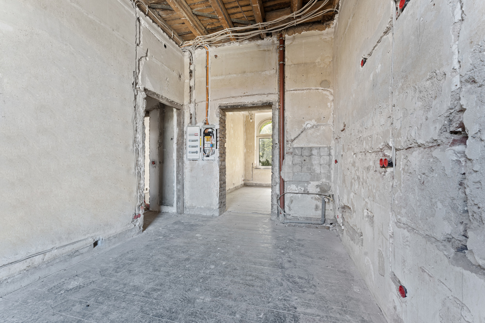 Ein leerer Raum in einer Wohnung im Rohbau mit sichtbaren Kabeln und unverputzten Wänden.