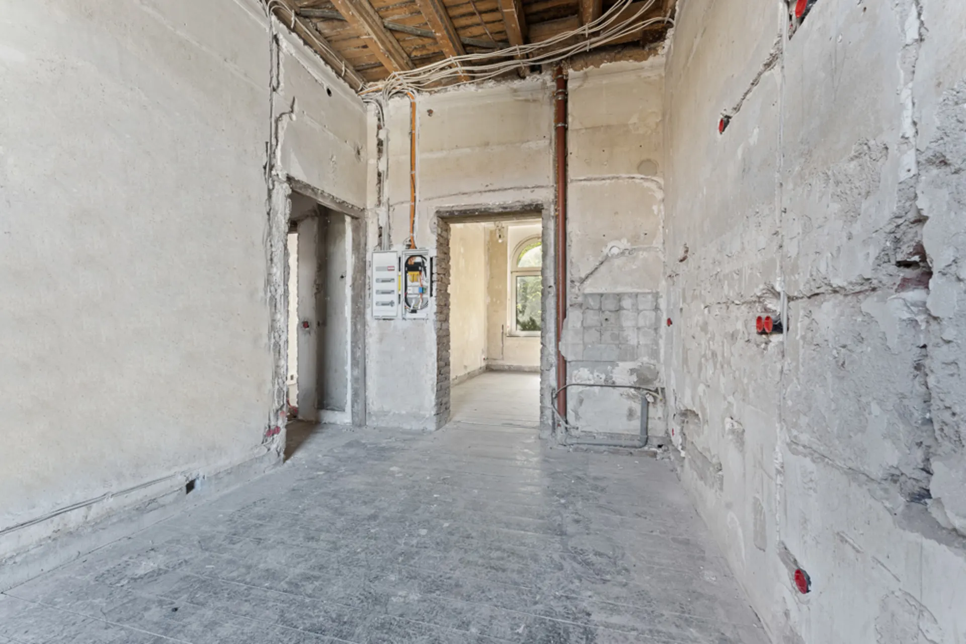 Ein leerer Raum in einer Wohnung im Rohbau mit sichtbaren Kabeln und unverputzten Wänden.