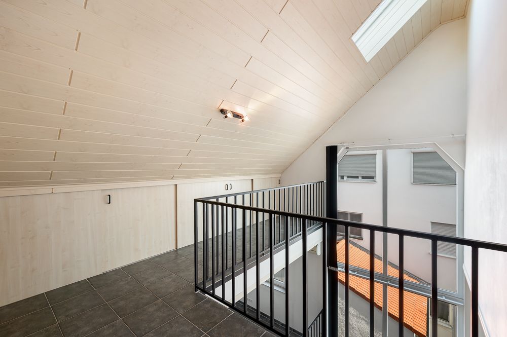 Heller Dachbodenraum mit schwarzem Geländer, Fliesenboden und Dachfenster.