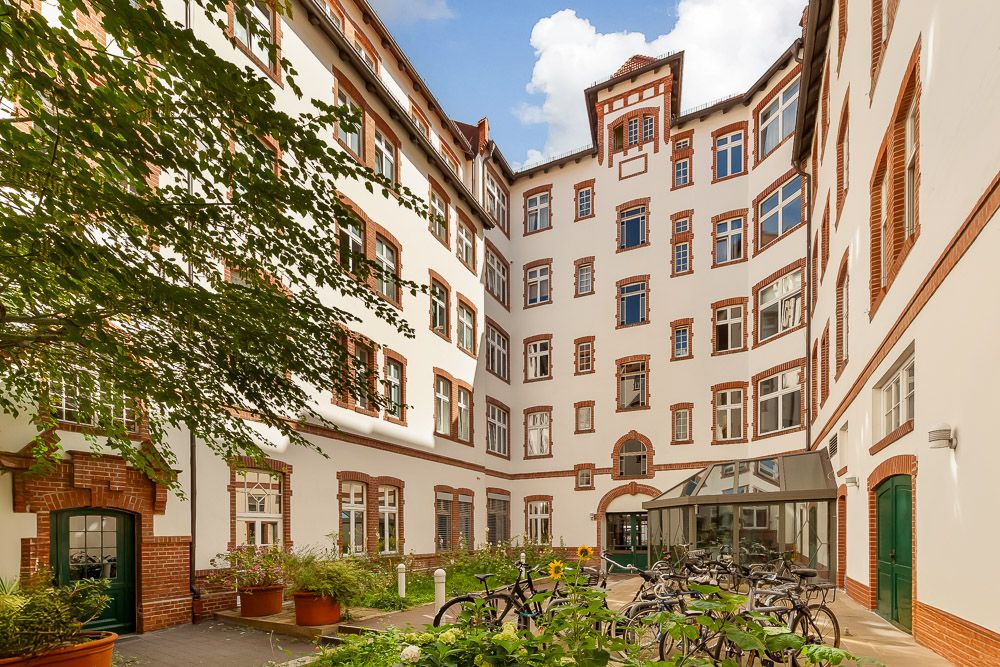 Innenhof eines Wohngebäudes mit Pflanzen, Fahrrädern und mehreren Fenstern.