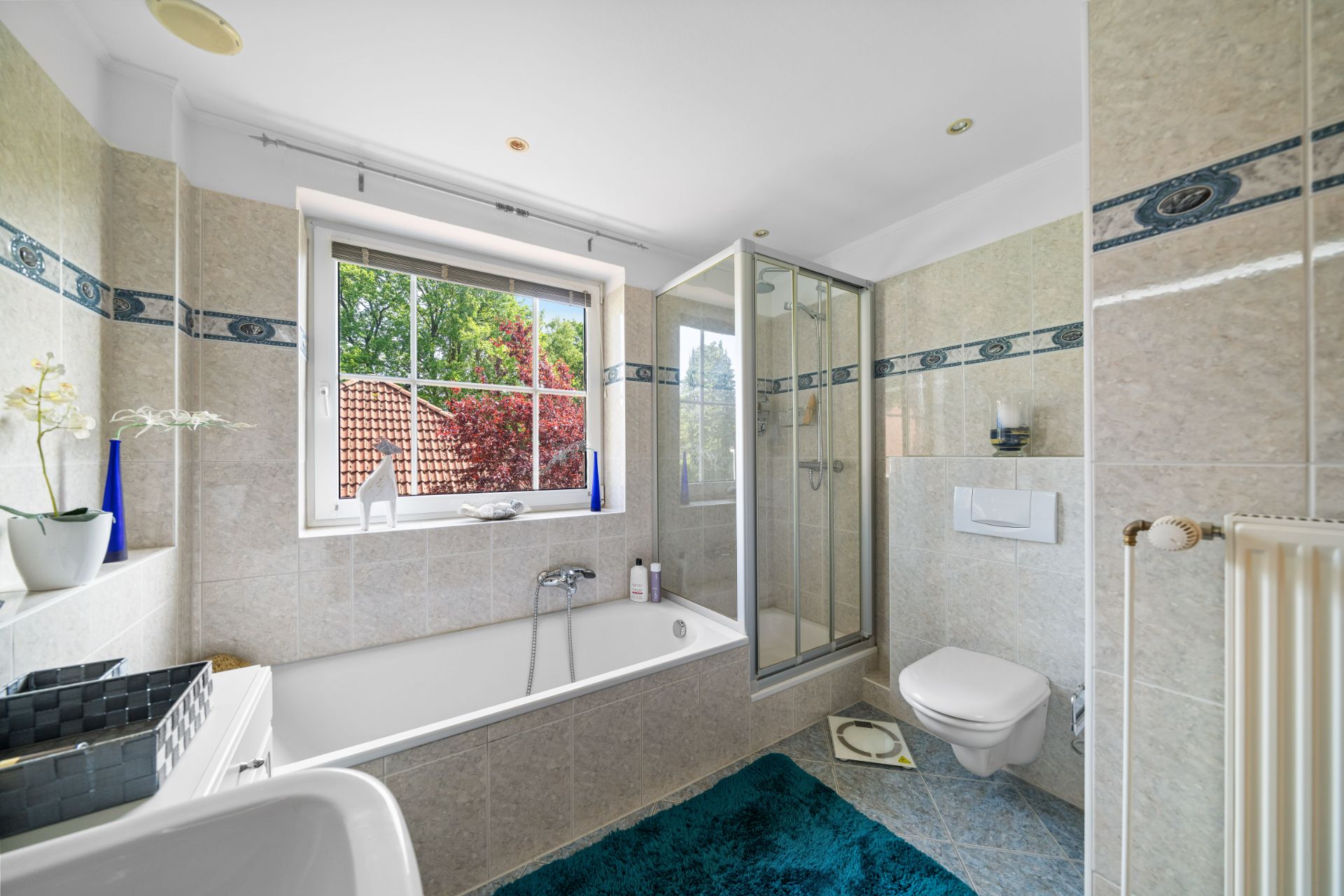 Helles Badezimmer mit Badewanne, Dusche, WC und großem Fenster mit Blick nach draußen.