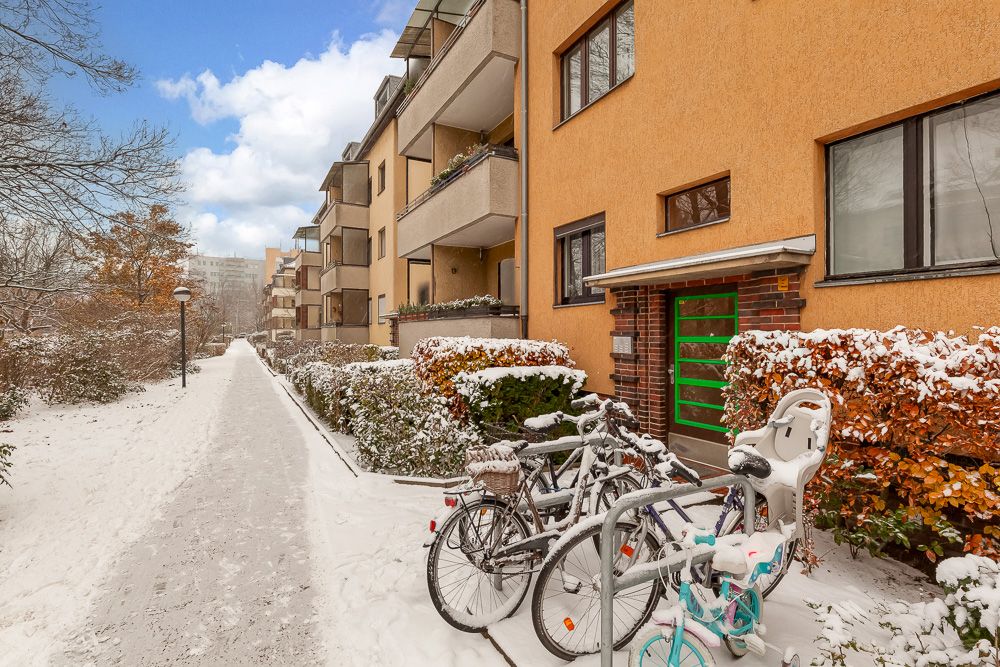 Mehrfamilienhaus mit Balkonen, verschneiter Gehweg und Fahrradständer mit Fahrrädern im Vordergrund.