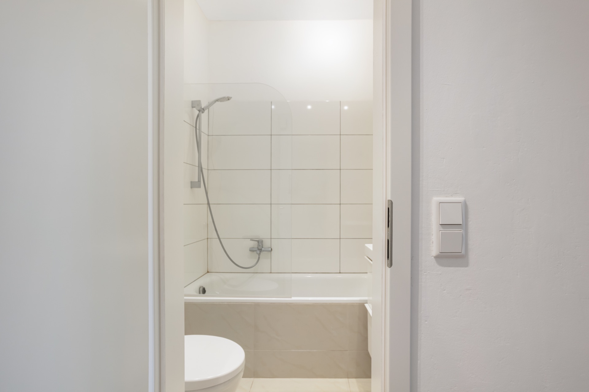 Modernes Bad mit Badewanne, Duschkopf und weißen Fliesen an der Wand.