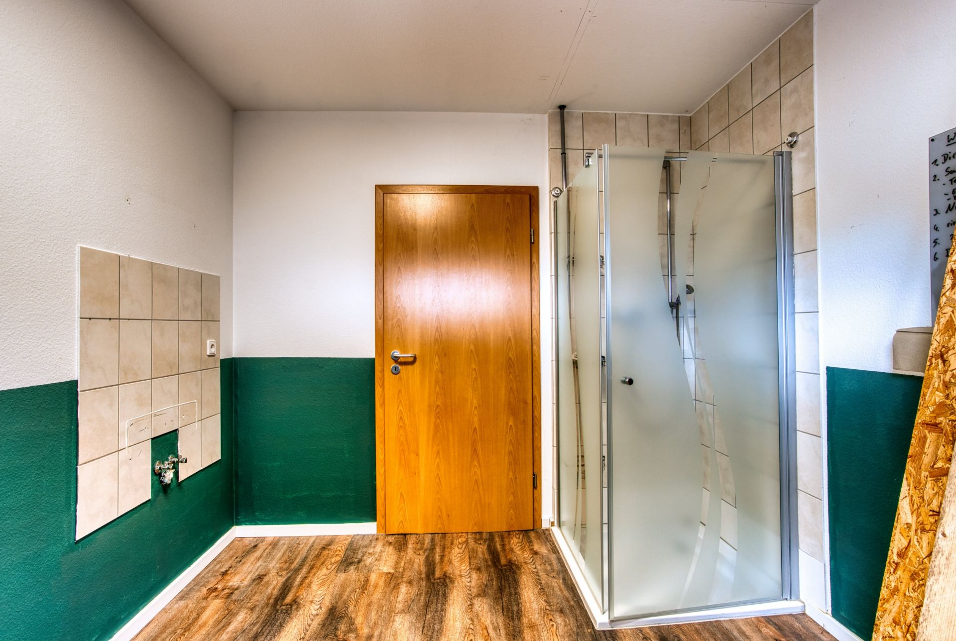 Badezimmer mit Holztür, Duschkabine und gefliestem Bereich an der Wand.