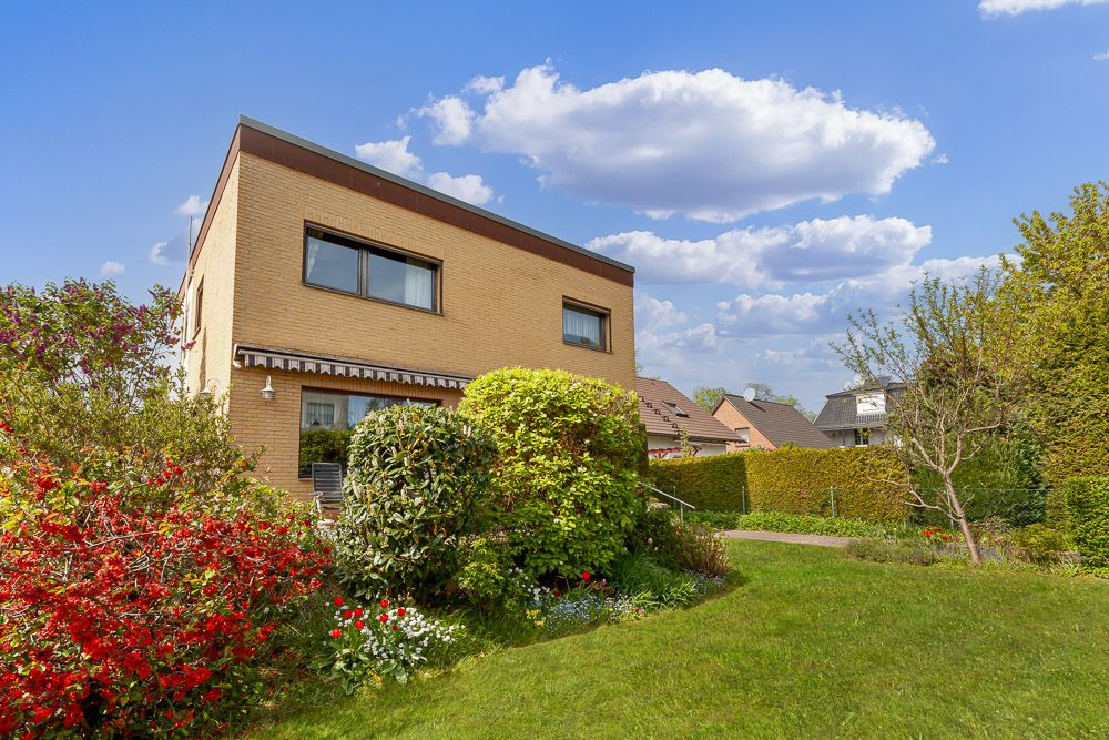 Modernes Wohnhaus mit großem Garten und vielen Büschen bei sonnigem Wetter.