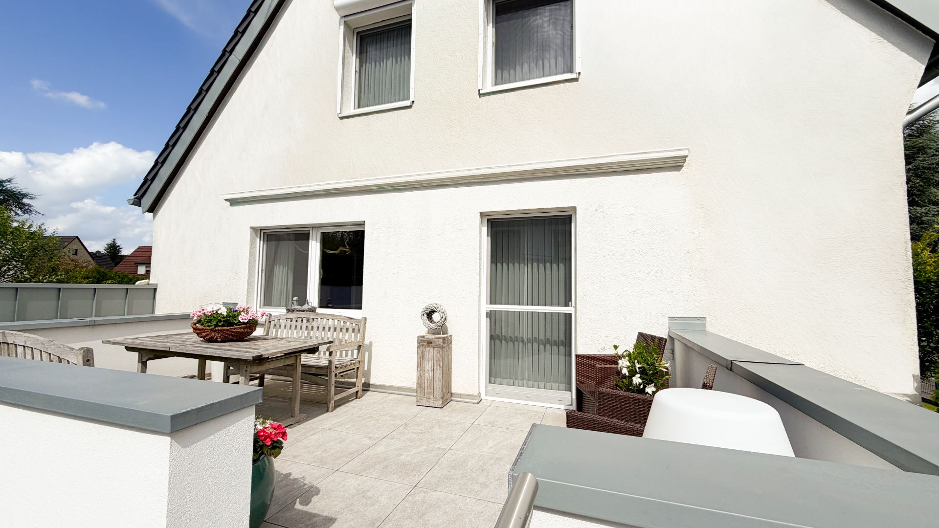 Große Terrasse mit Sitzgruppe und Pflanzkübeln vor einem weißen Wohnhaus.