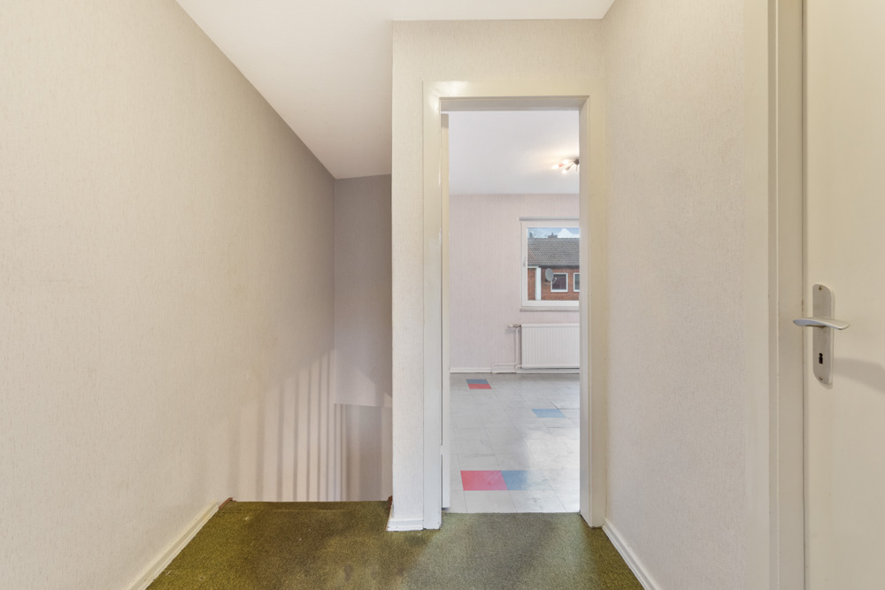 Flur mit Treppe und offenem Durchgang zu einem hellen Raum mit Fenster.