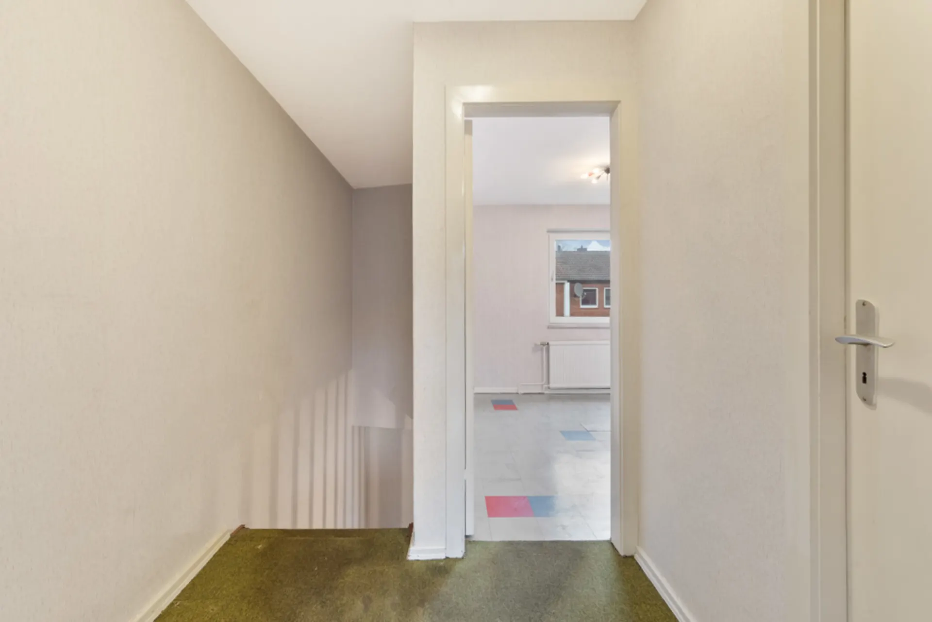 Flur mit Treppe und offenem Durchgang zu einem hellen Raum mit Fenster.
