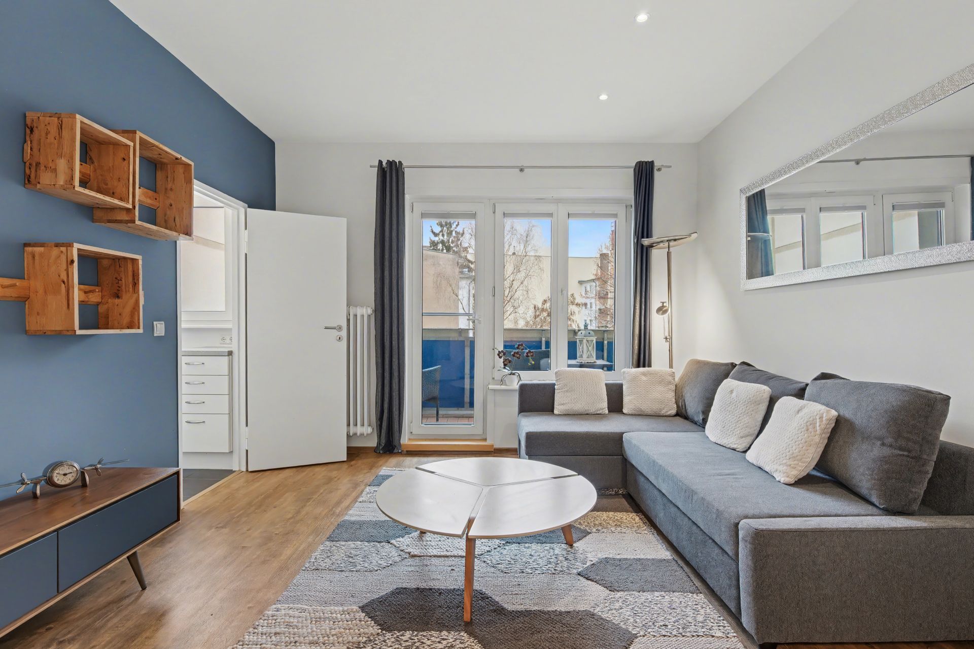 Modernes Wohnzimmer mit grauem Sofa, rundem Tisch, blau-weißer Wand und großem Fenster.