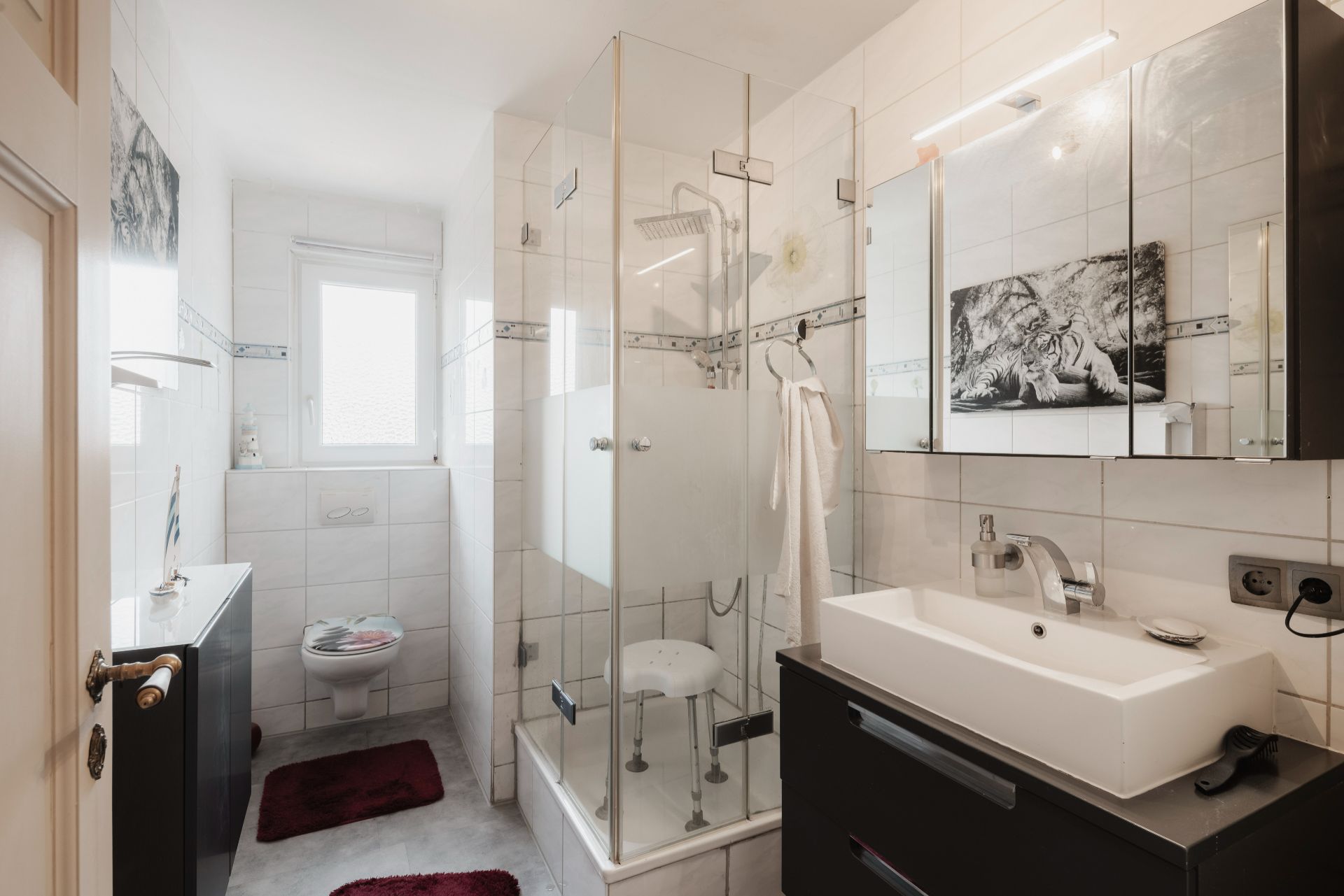 Modernes Badezimmer mit Glasdusche, Waschbecken, Spiegel und WC, weiß gefliest.
