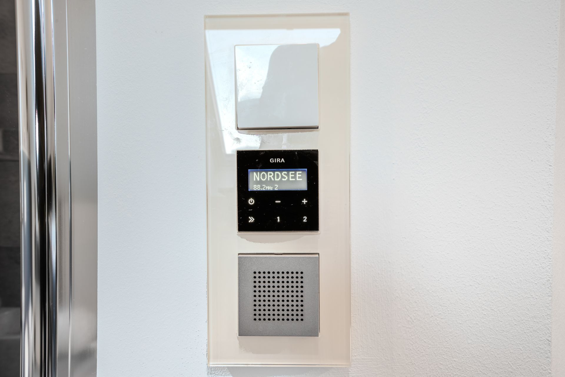 Nahaufnahme einer Wandbedienung mit Display, Lautsprecher und Tasten, Anzeige mit dem Text 'NORDSEE'.