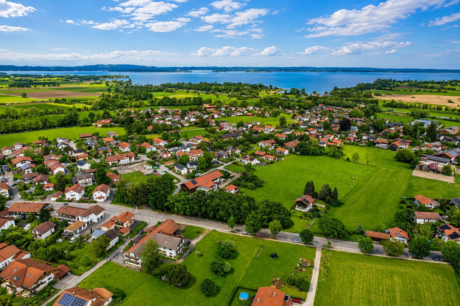 Luftaufnahme einer Wohnsiedlung mit vielen Häusern, grünen Flächen und einem See im Hintergrund.